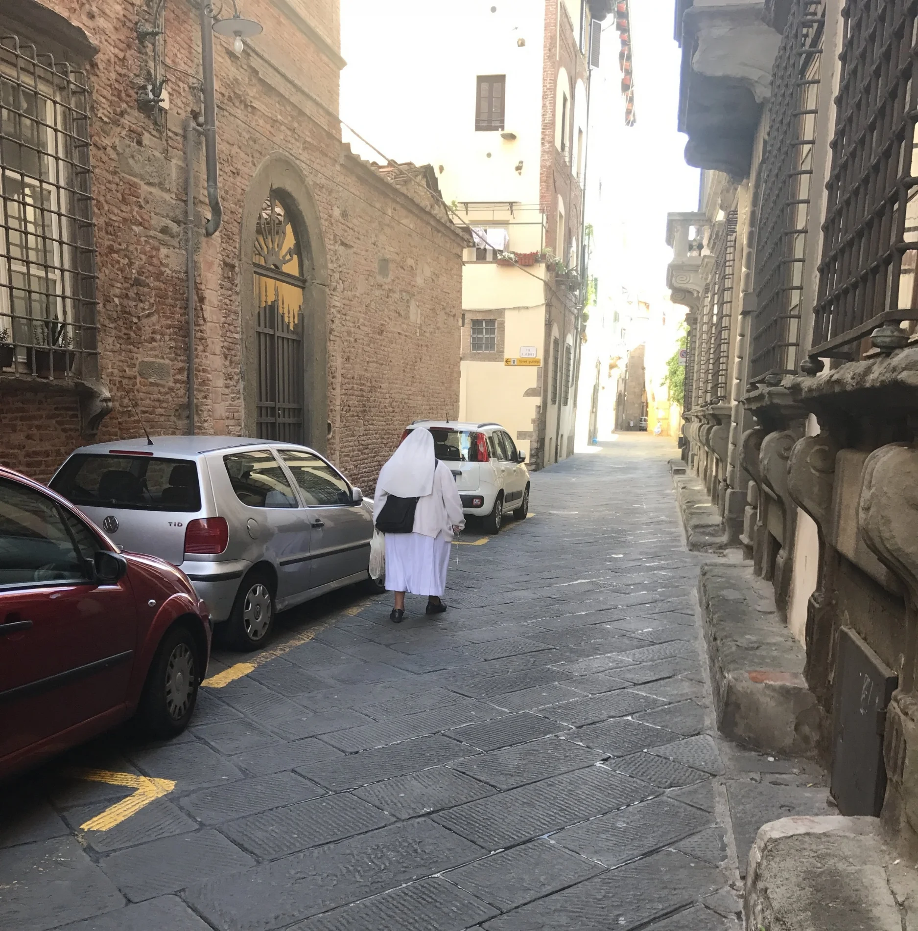 A nun walks toward a sun-splashed area of town.