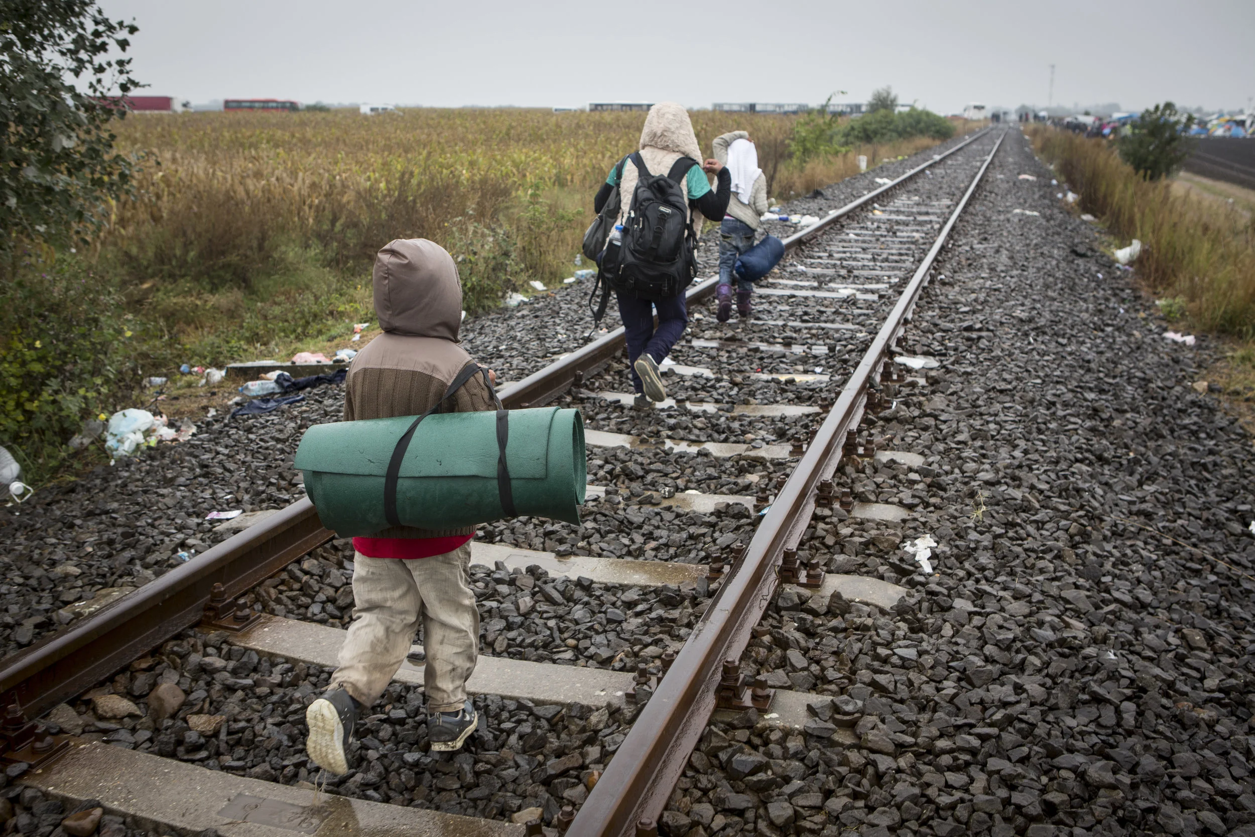 Three refugees walk along the train tracks running from Serbia into Hungary on their way to Austria