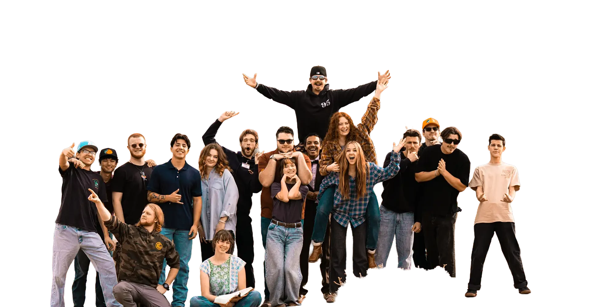 A large group of young people posing together outdoors, some smiling and making various hand gestures, with one person being lifted above the others.