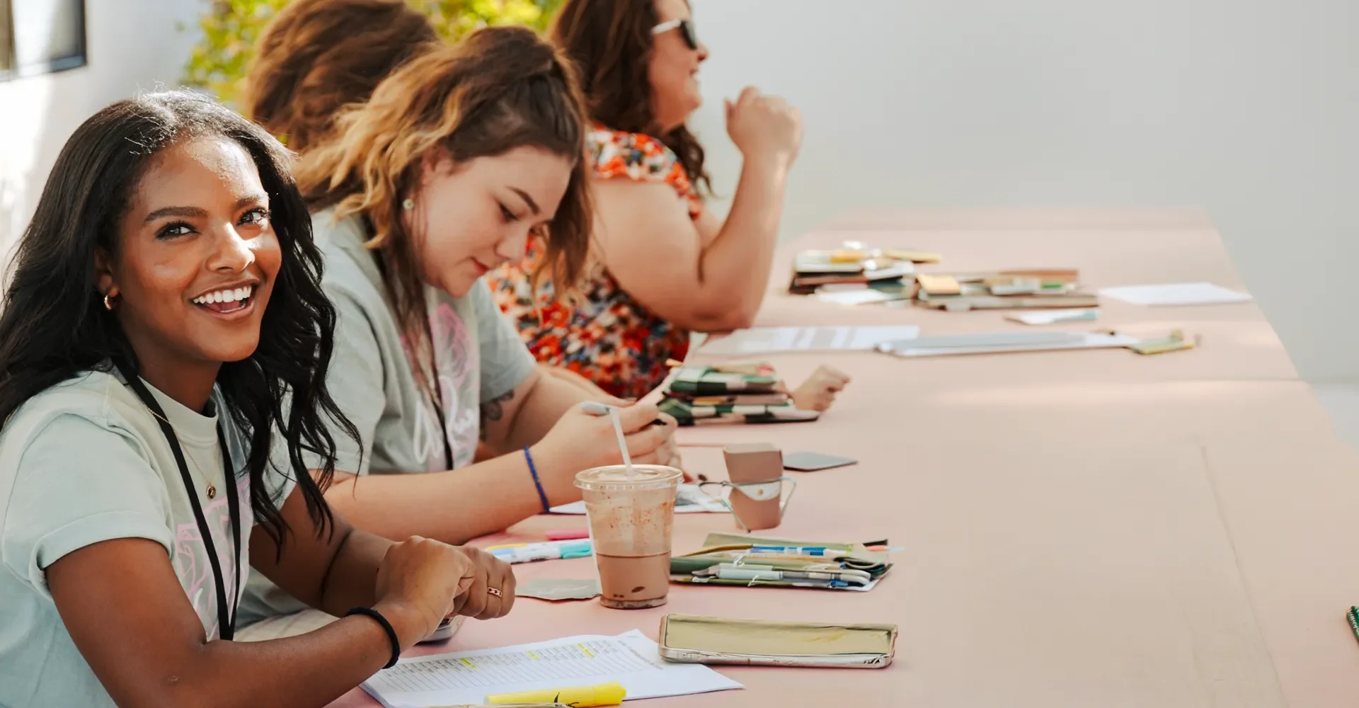 Group of women sitting at a table, smiling and engaging in a discussion, with notebooks, pens, and drinks in front of them.