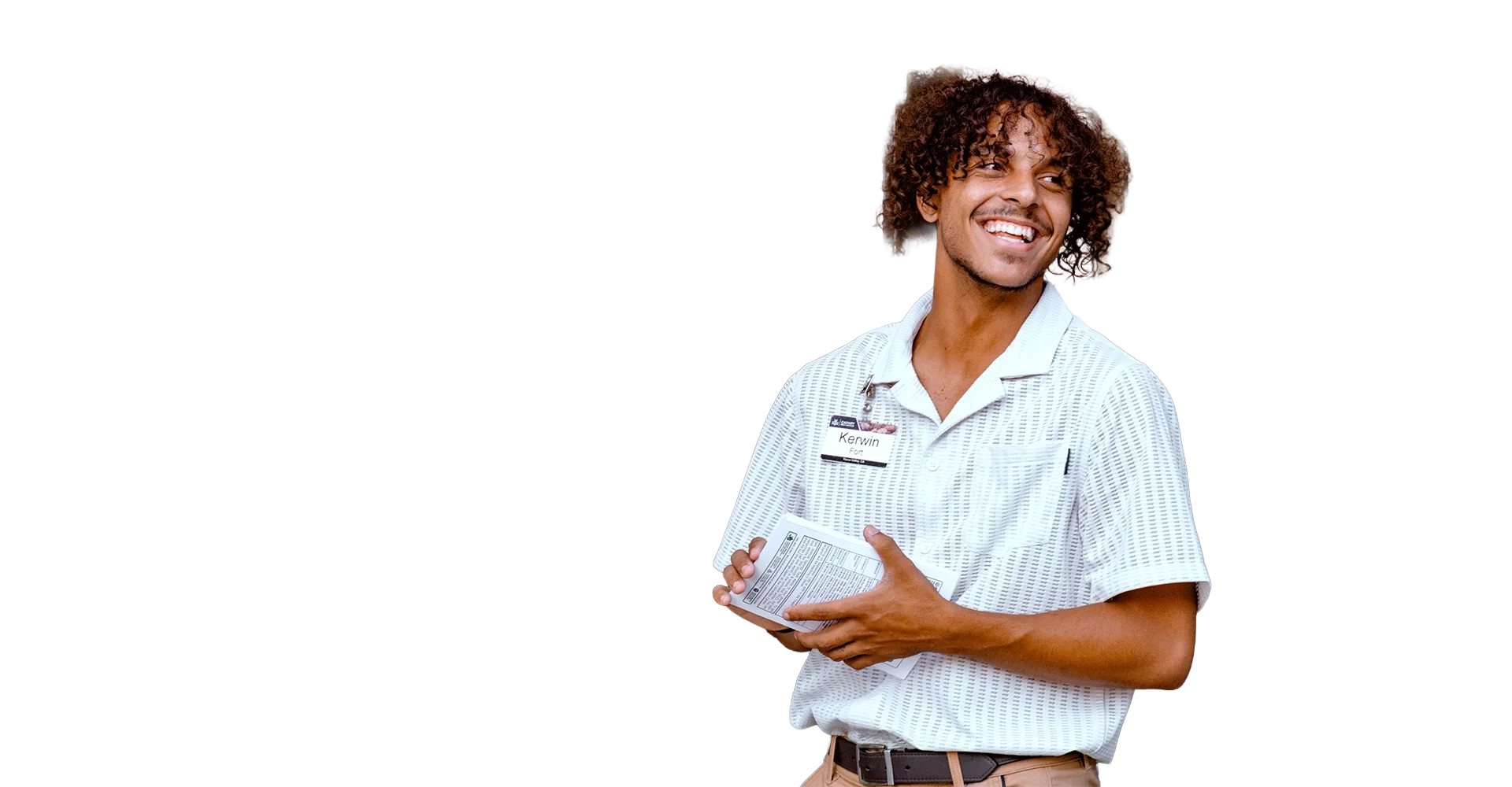 A cheerful man with curly hair wearing a name tag and a white striped polo shirt, holding a box of medication, standing against a plain background.