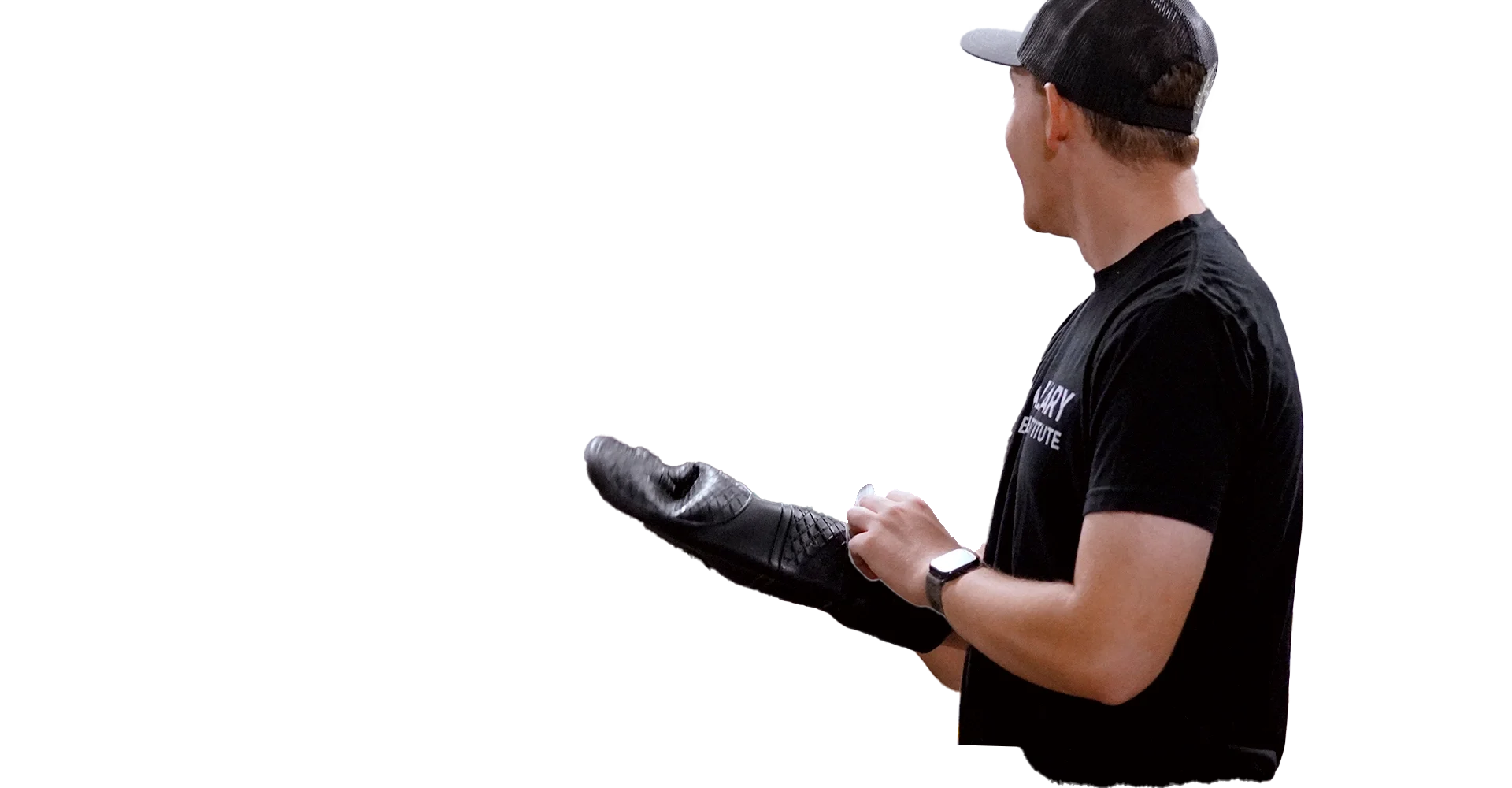 A man in a black t-shirt and black baseball cap is wearing a black glove on his left hand, holding a small object, and wearing a fitness tracker on his right wrist.