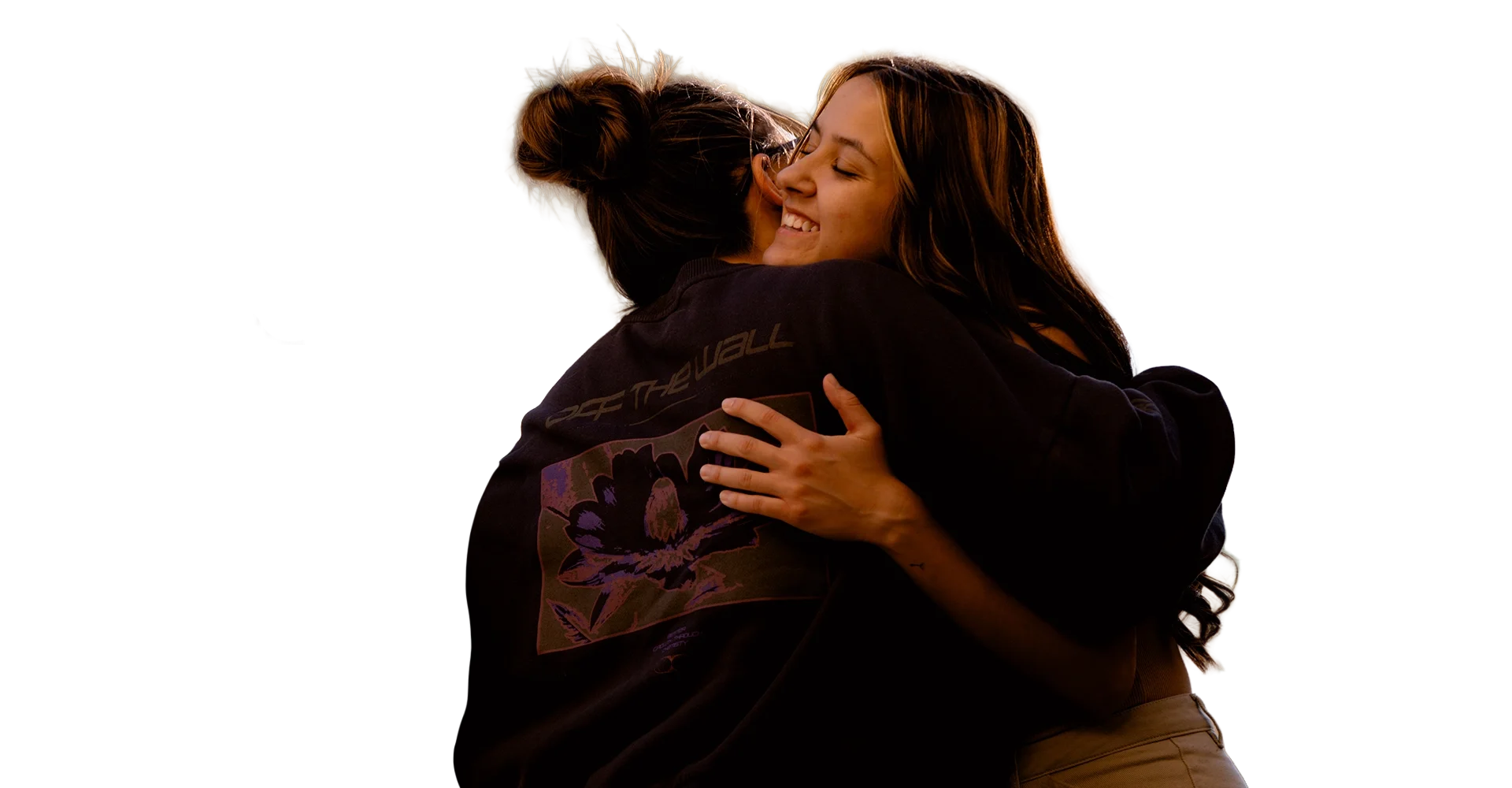 Two women hugging warmly with eyes closed, smiling, and embracing tightly outside on a sunny day.