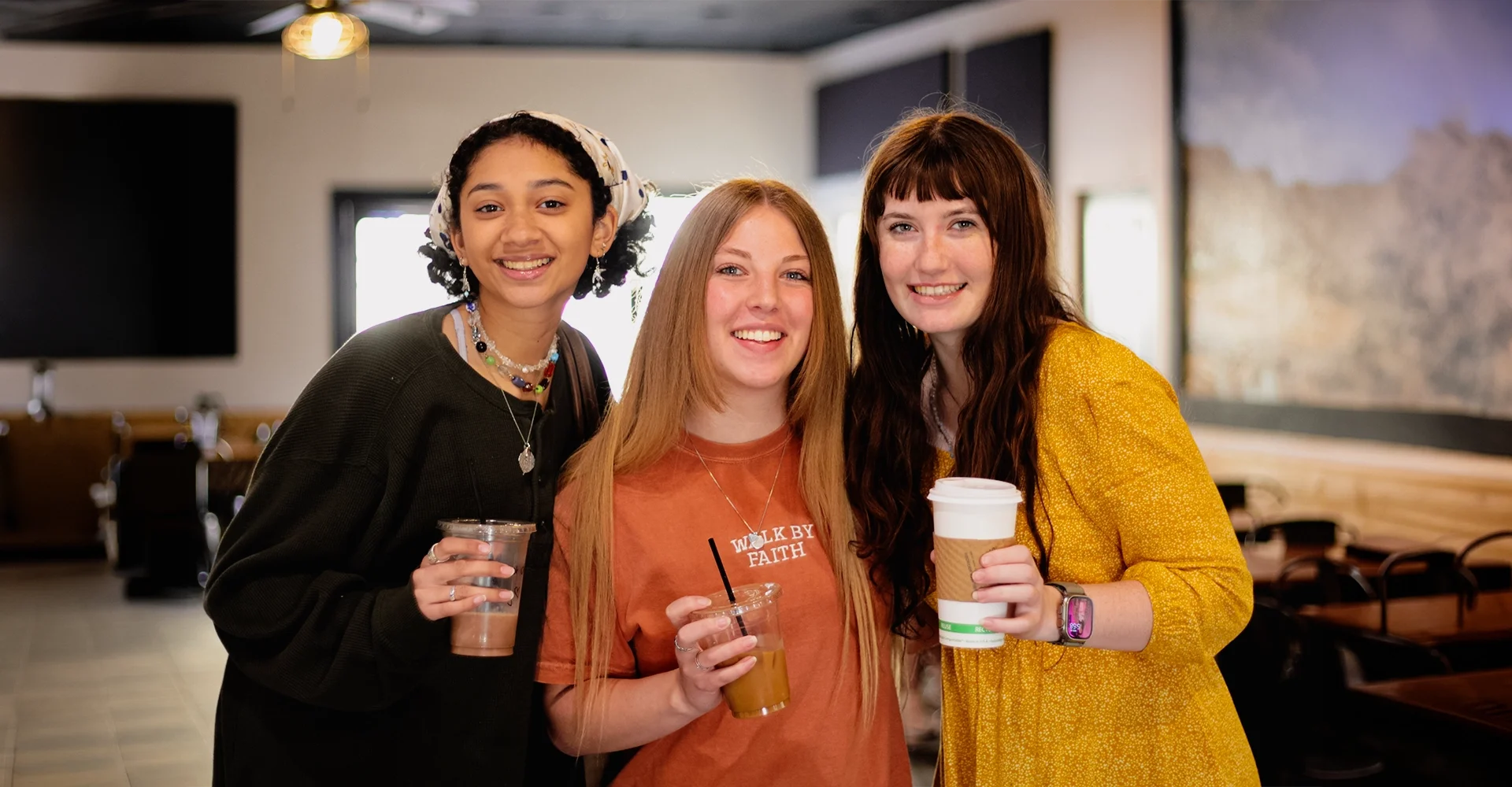 Three young women smiling and holding drinks in a cafe or restaurant.