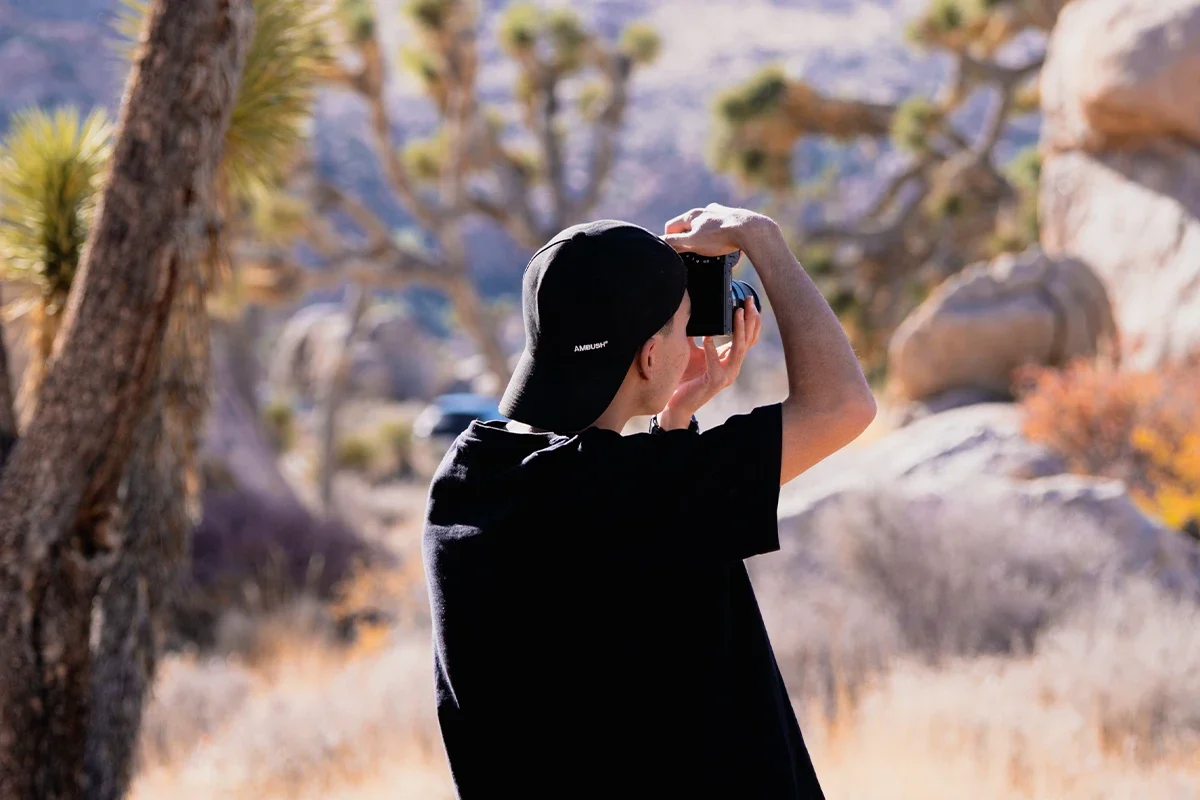 A person taking a photo with a smartphone in a desert landscape with trees and rocks.