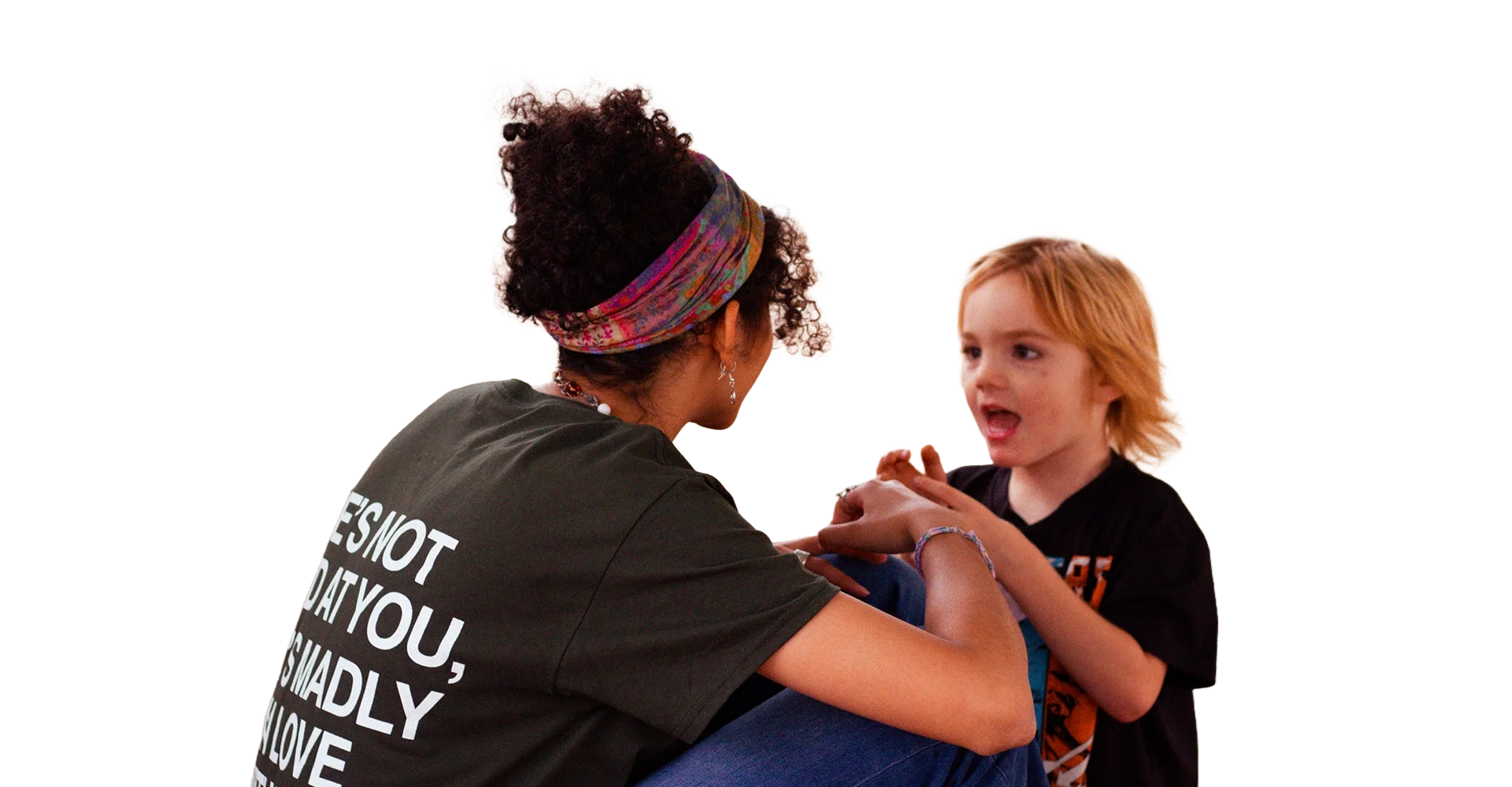 A woman and a young boy engaging in a conversation indoors, with the woman wearing a headband and a dark T-shirt, and the boy speaking animatedly with red hair.
