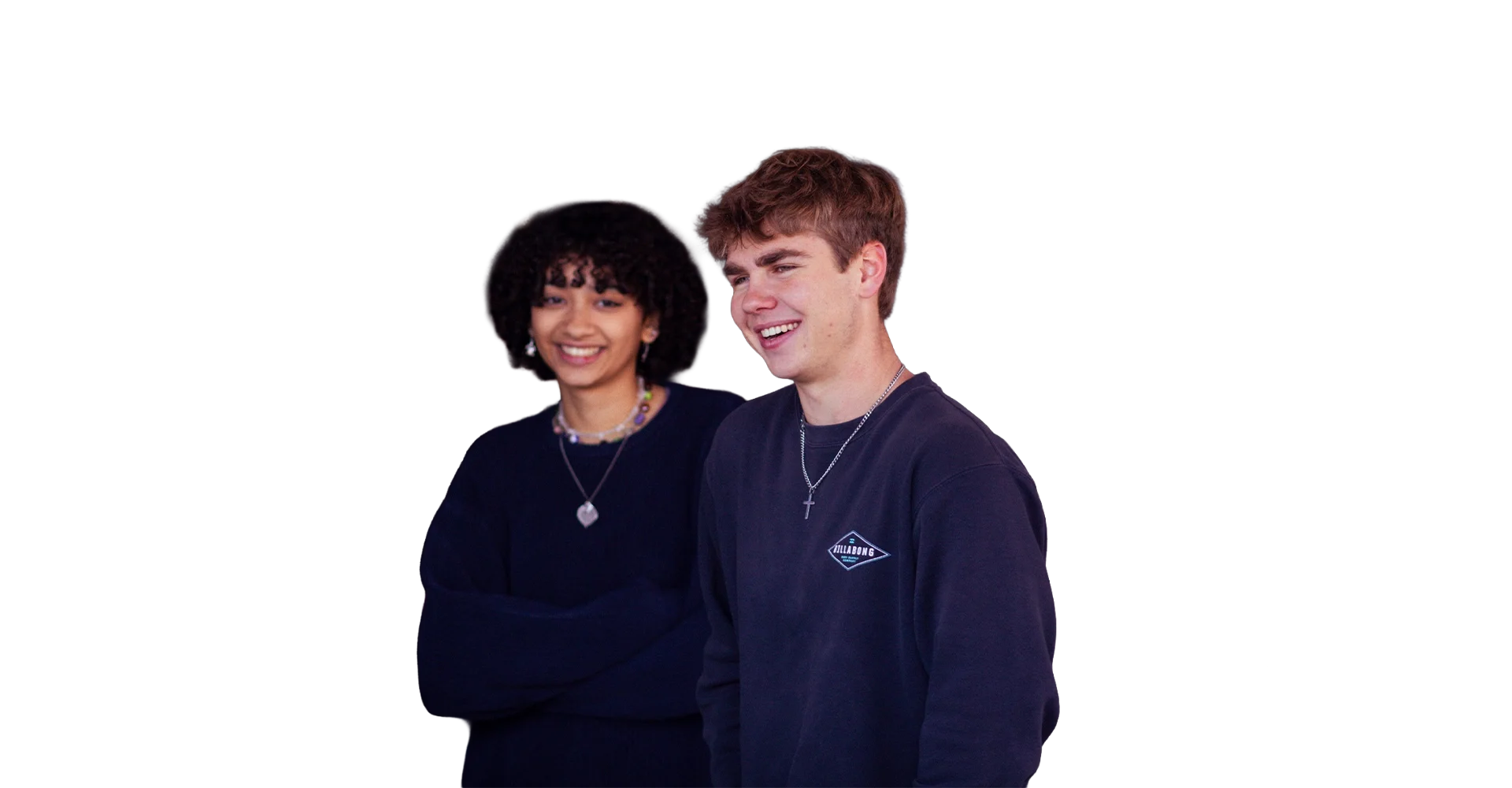 Young man and woman smiling, standing close together, wearing dark casual clothes with necklaces, against a plain white background.