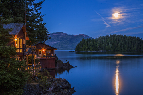 image of a waterfront home at night with the moon in the sky