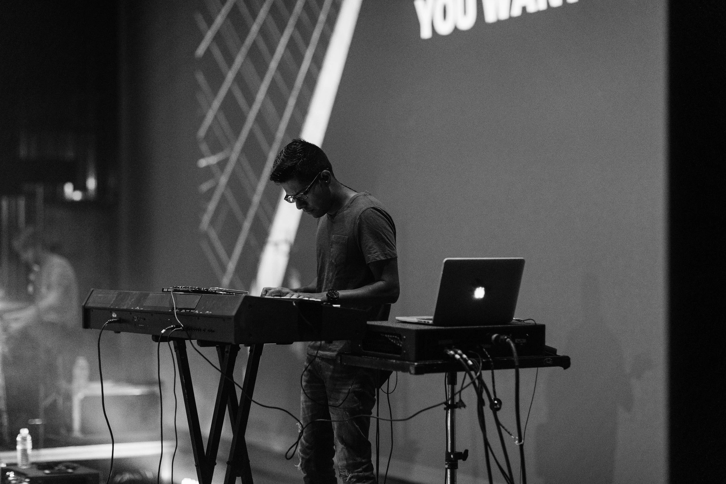 black and white image of piano player playing keyboard using a laptop to get his sounds & patches