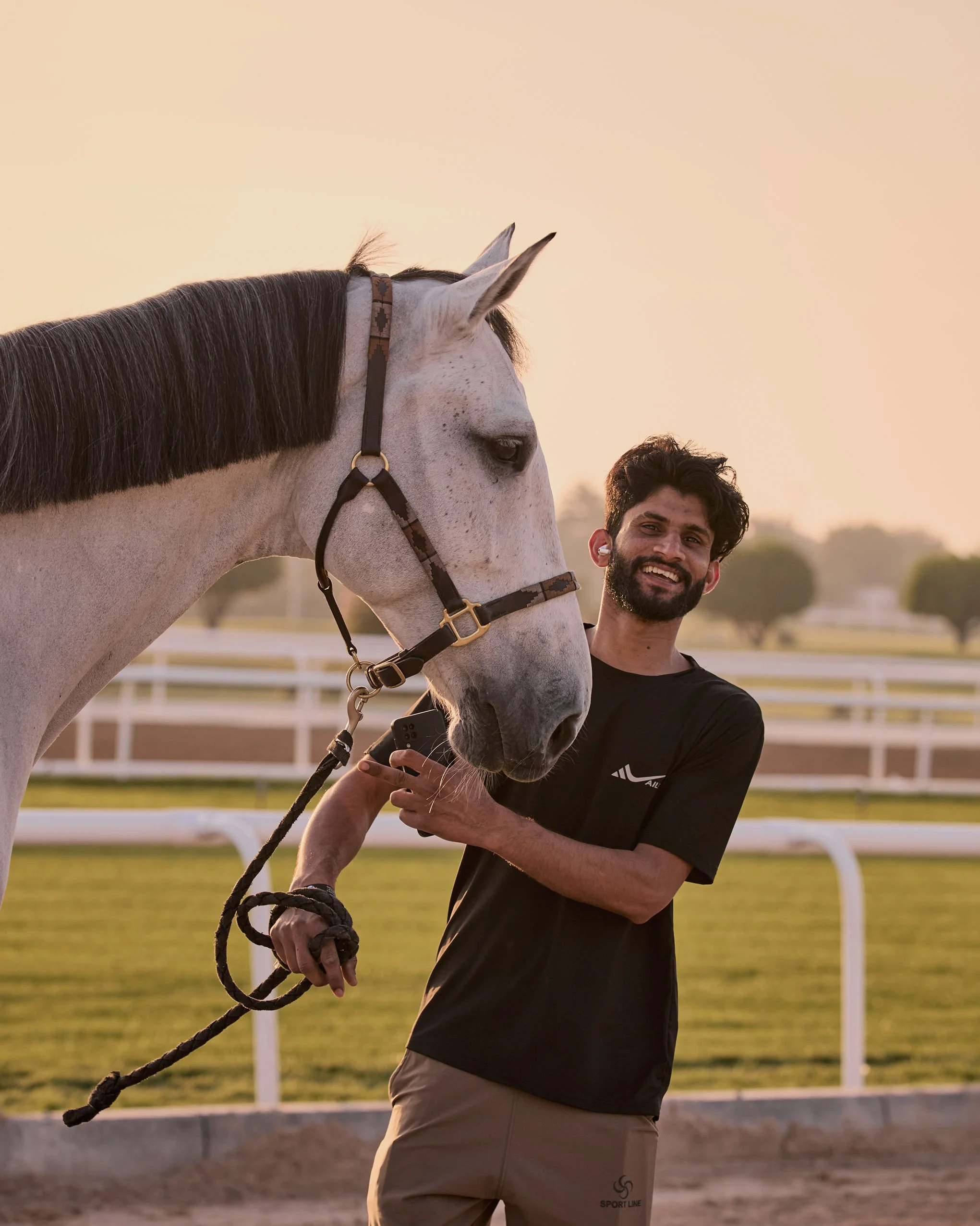 A groom laughing with a horse in golden light