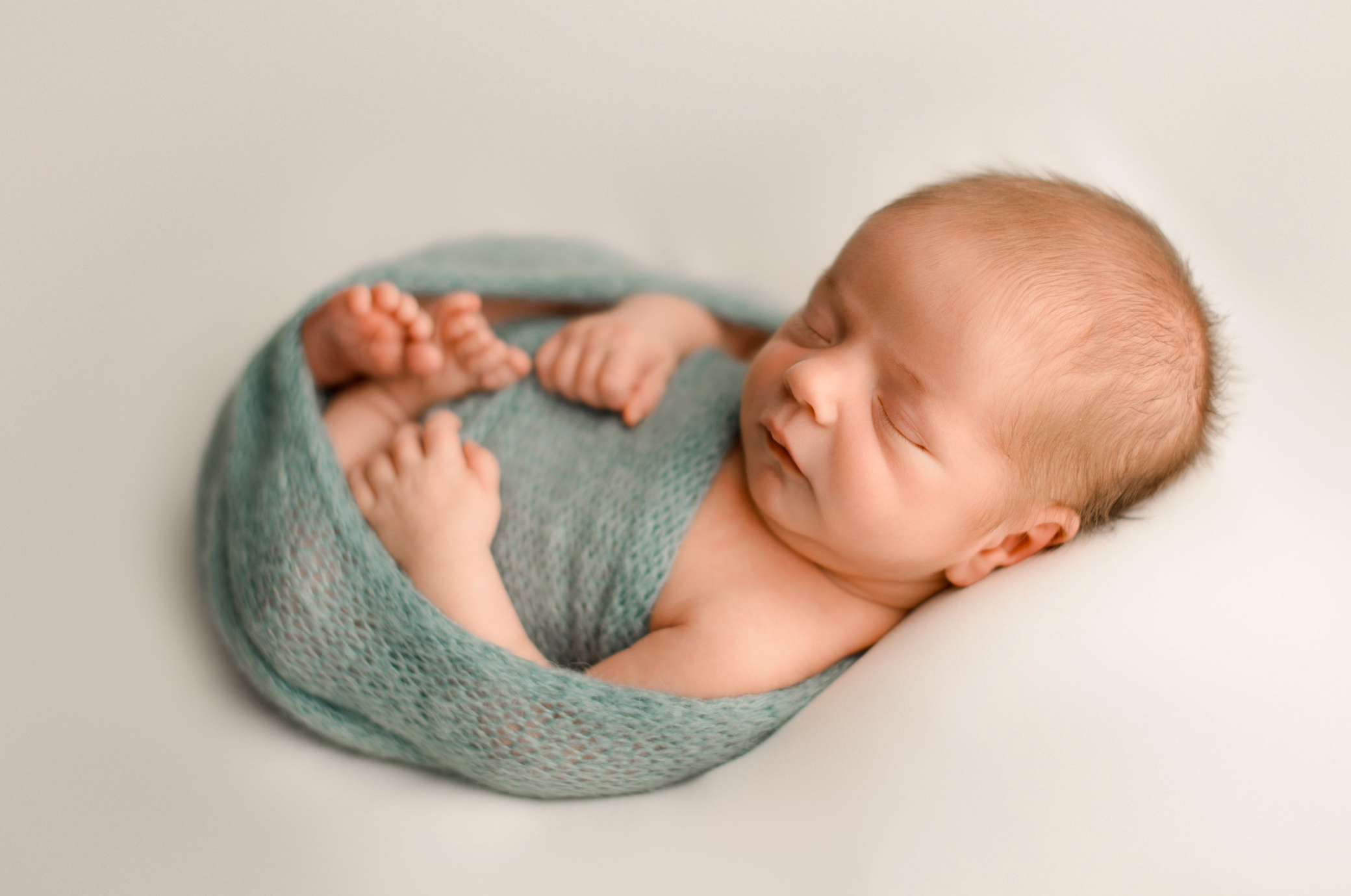 Newborn baby boy wrapped in light blue knit wrap on neutral fabric in the photo studio.