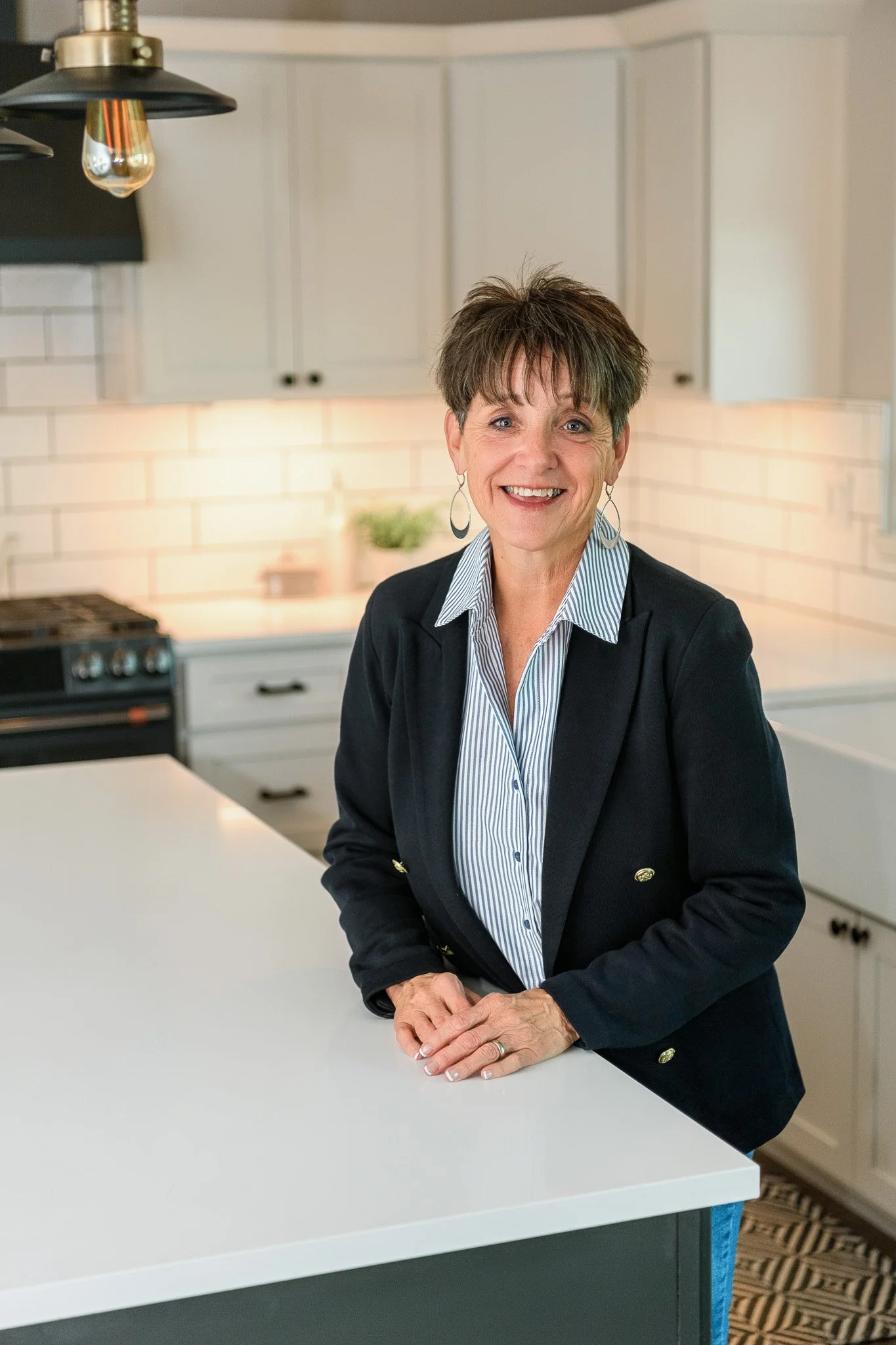 A woman smiling and standing in a modern kitchen with white cabinets and a white countertop.