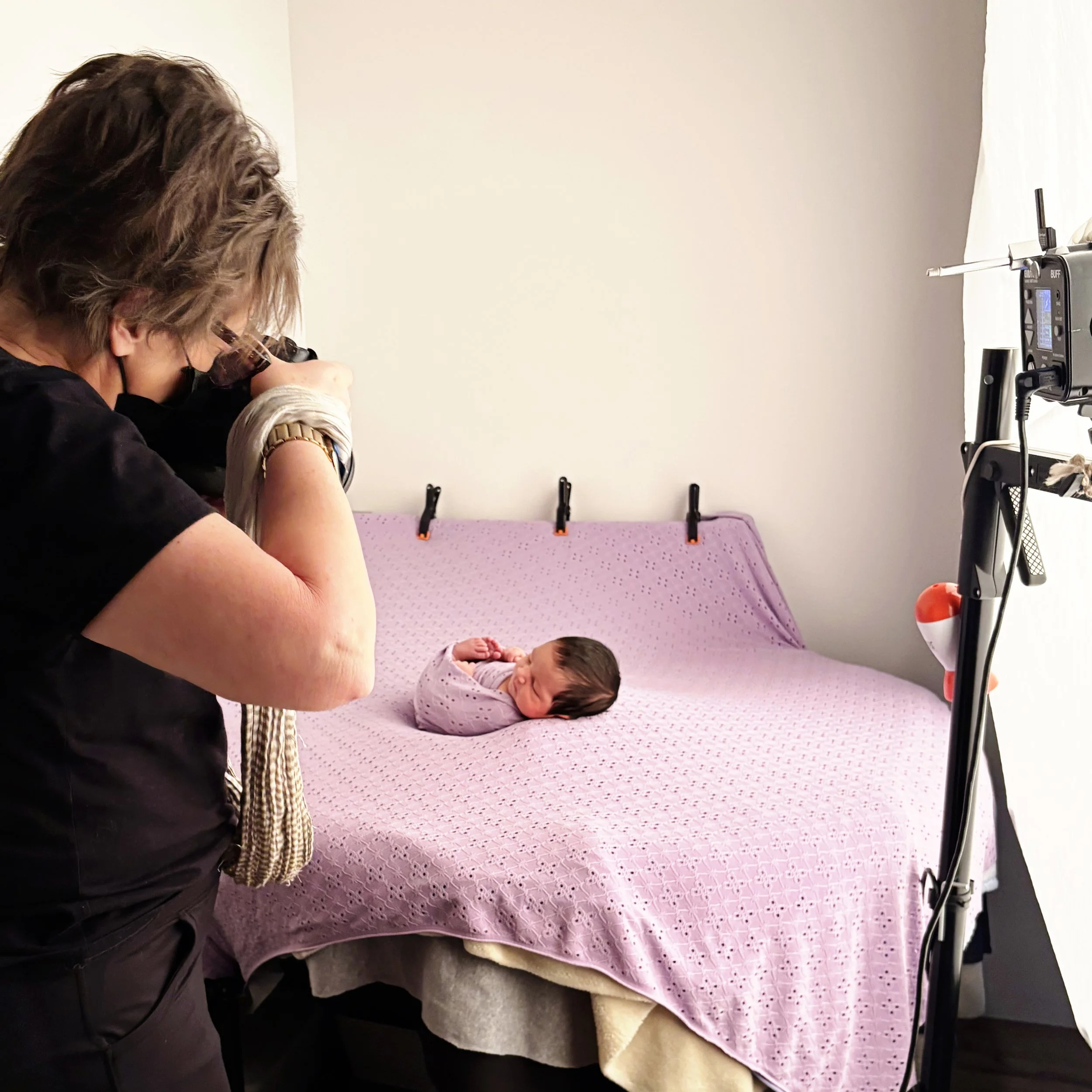 A photographer taking a picture of a newborn baby lying on a pink bedspread in a studio setting.