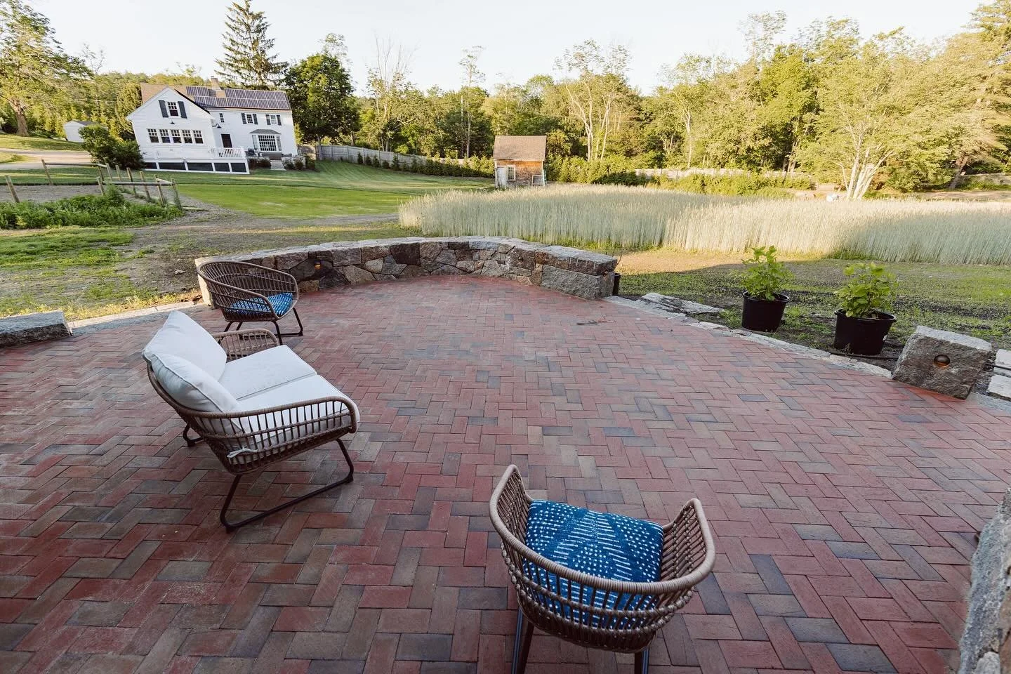 Before & After: 
This cozy back patio space is tucked in by seat height stone walls that curve around it and a larger stone wall to support the stairs down from the side entry. A herringbone brick pattern that flows from wall to wall. Eventually