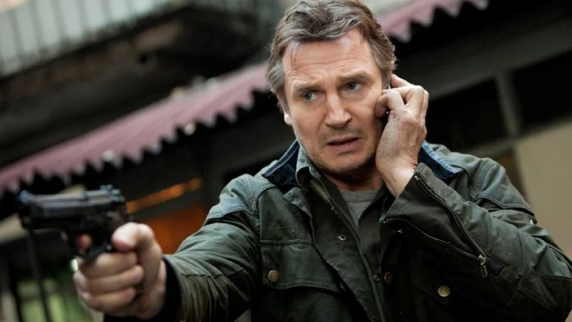 Liam in peak action dad form, one hand on the gun, the other on a cell phone.