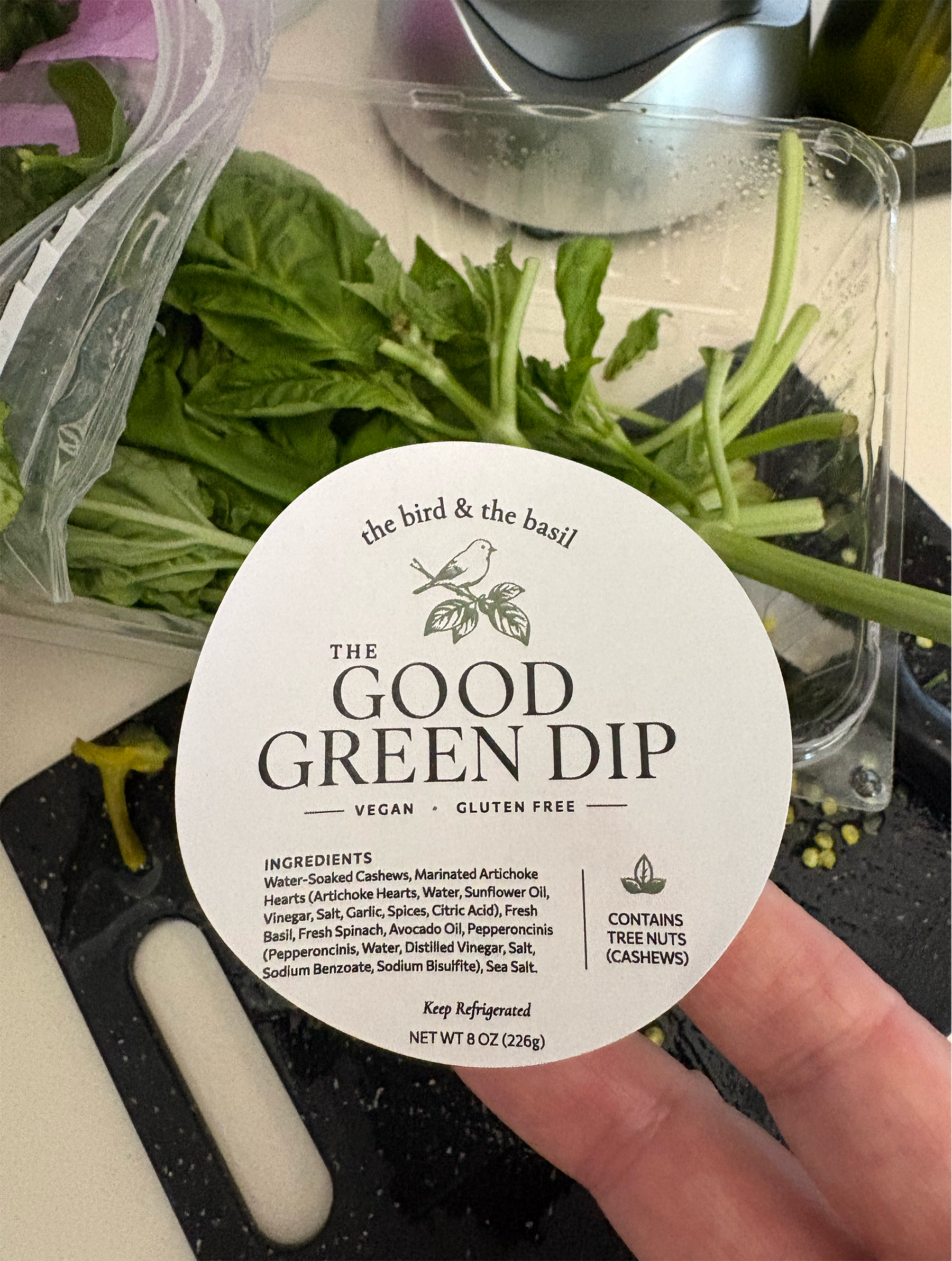 The good green dip label in hand with bag of spinach in the background