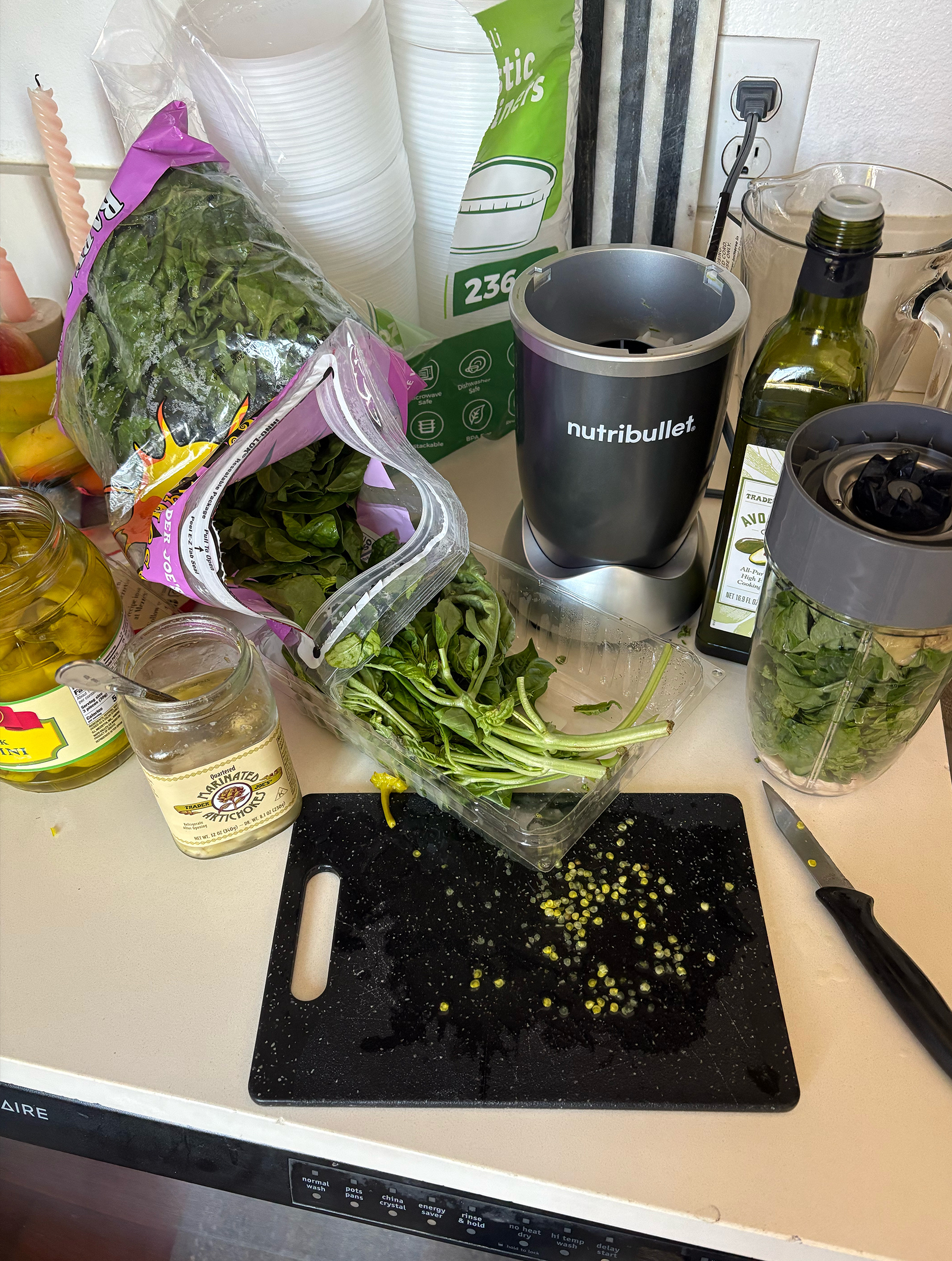 Spinach, basil, bowl of soaked cashews, bowl of marinated artichoke hearts, pepperocinis on white kitchen counter