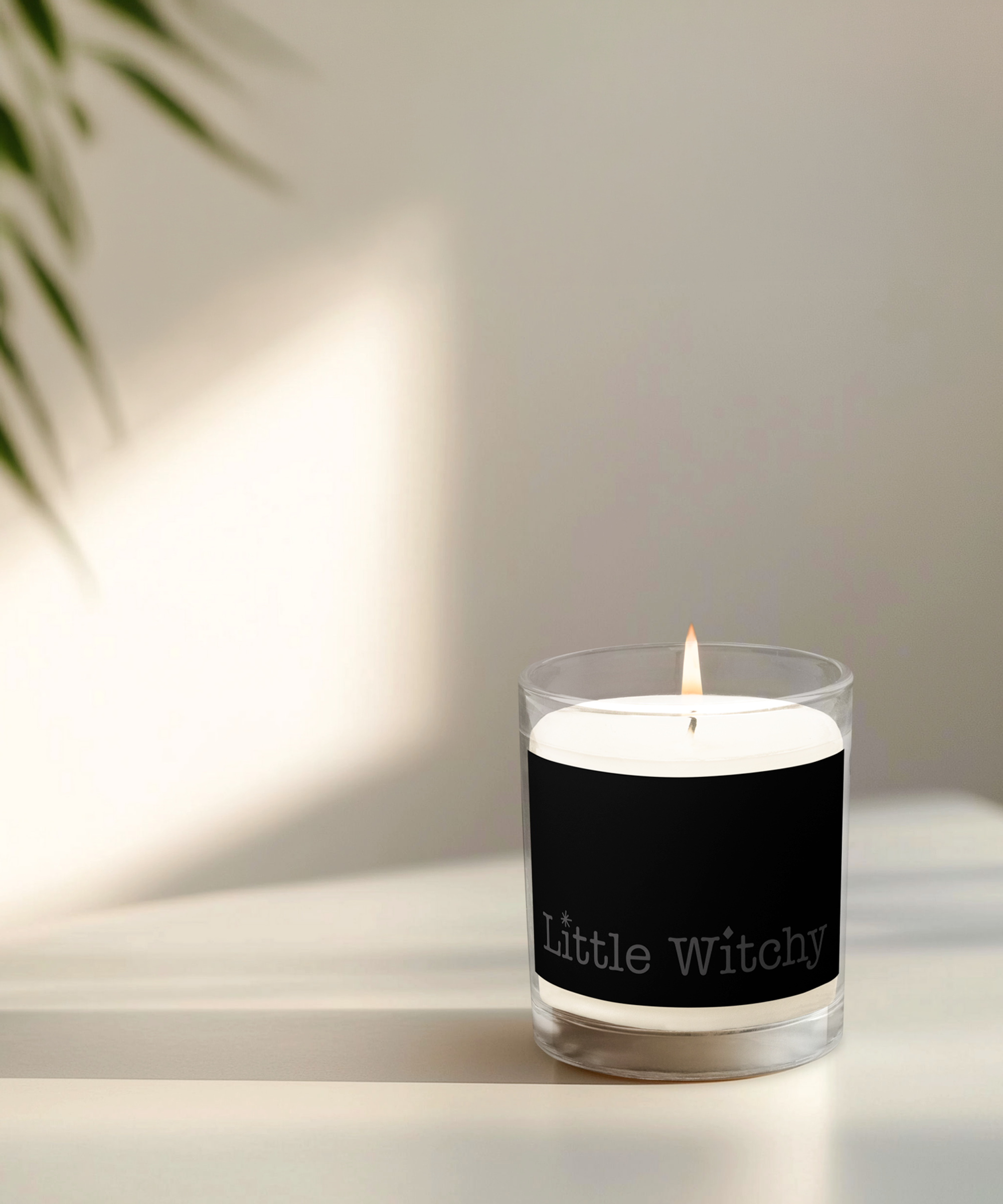 Little Witchy Candle Lit on a table, beige colored with plant in background and sunlight coming in