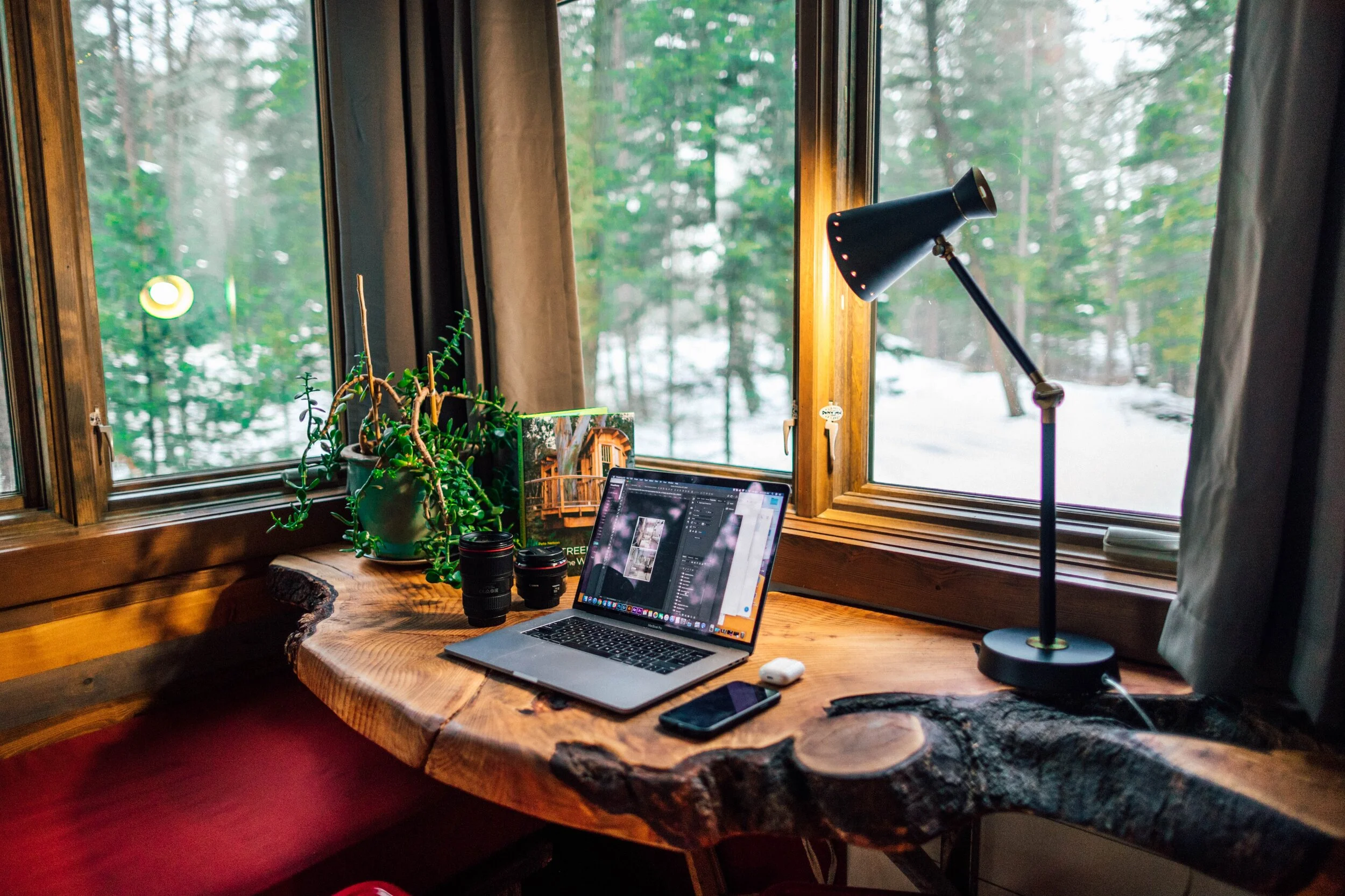 A home office desk in rustic log-cabin tones and a view of snowy pine trees through the window.