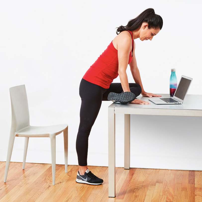 A woman is showing a modified pigeon pose at her desk.