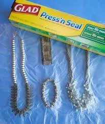 Lay out a piece of cling wrap sticky part up. Place all necklaces and bracelets on half of the piece of wrap and then fold it over and secure it.
