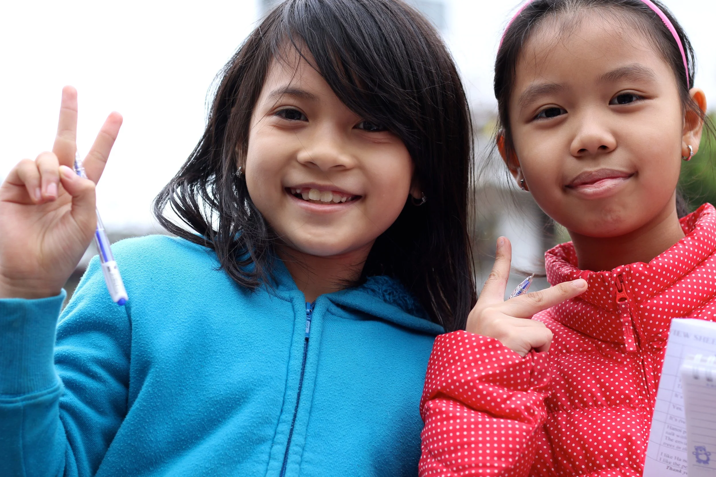 Two young girls practicing their English, pen and paper in hand.