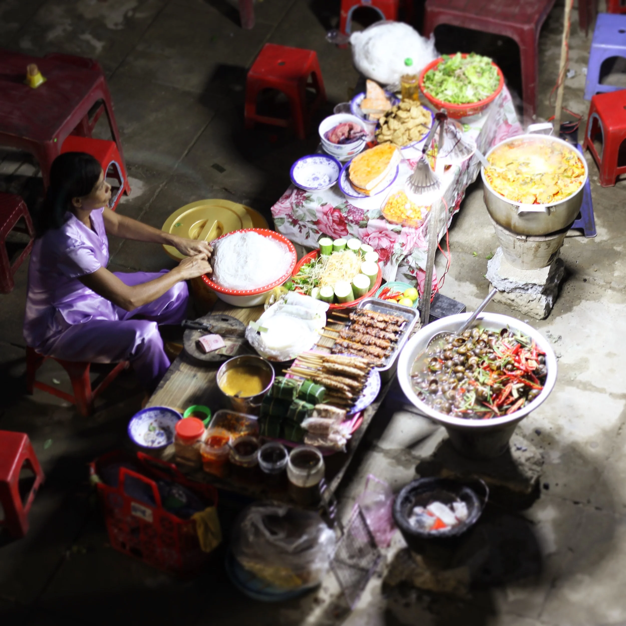 A woman cooking at her colorful street stand at night in Hue.