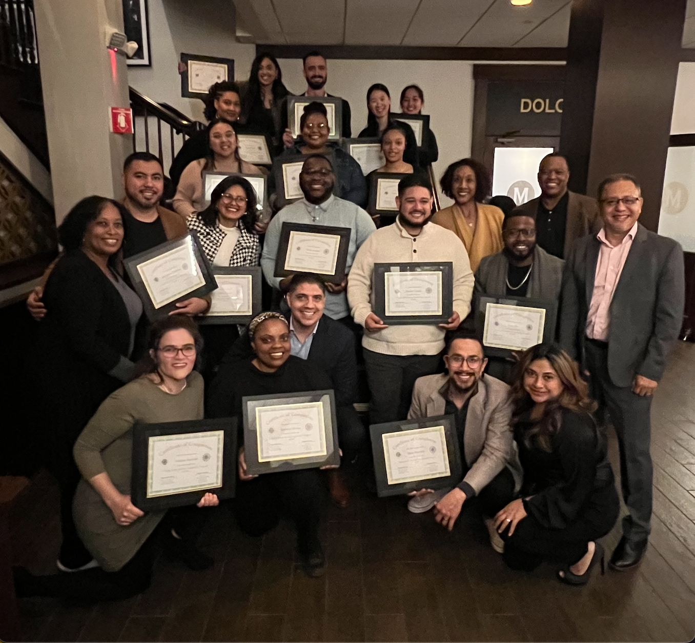 Group of diverse people holding framed certificates at an awards ceremony or graduation event.