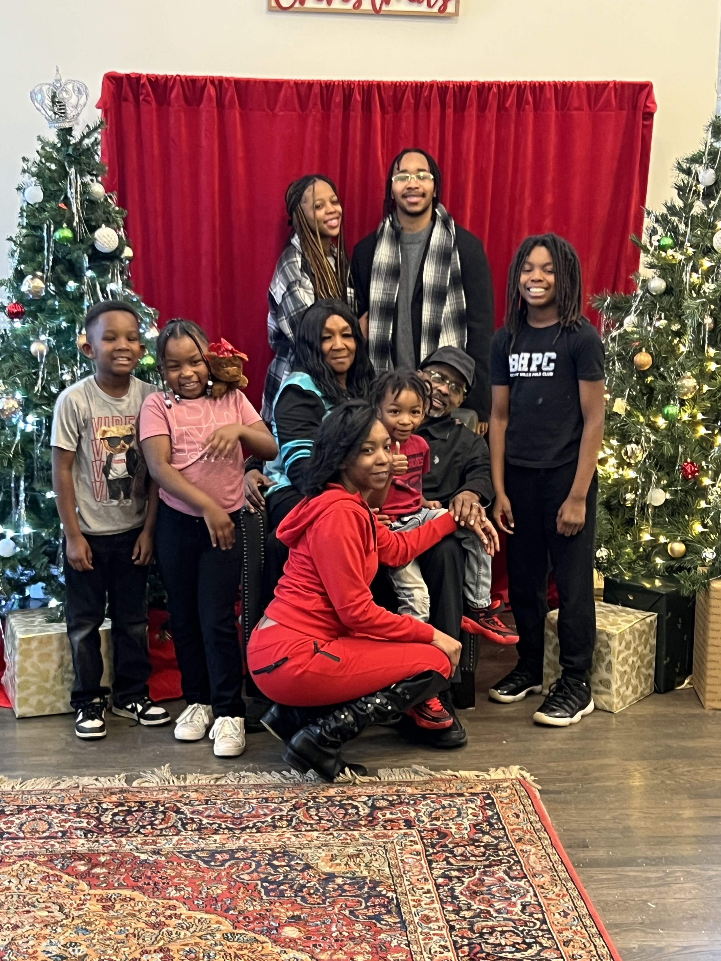 A family gathering during Christmas, with children and adults posing in front of decorated Christmas trees and red curtains.