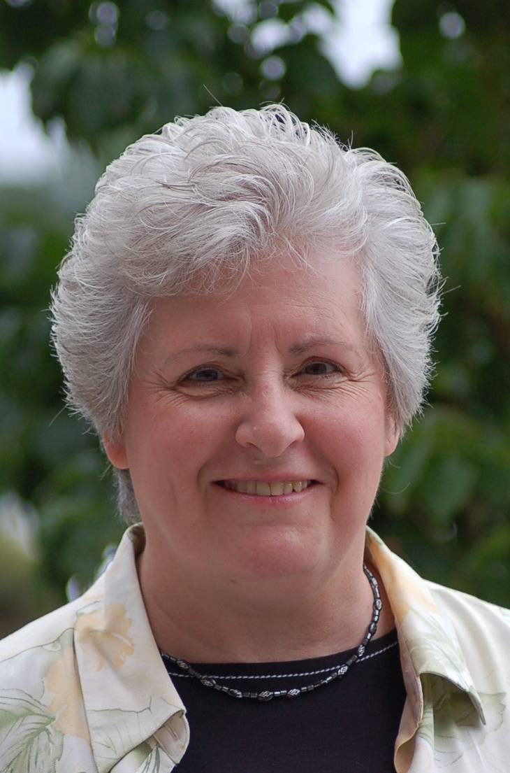A smiling woman outdoors with green foliage in the background.