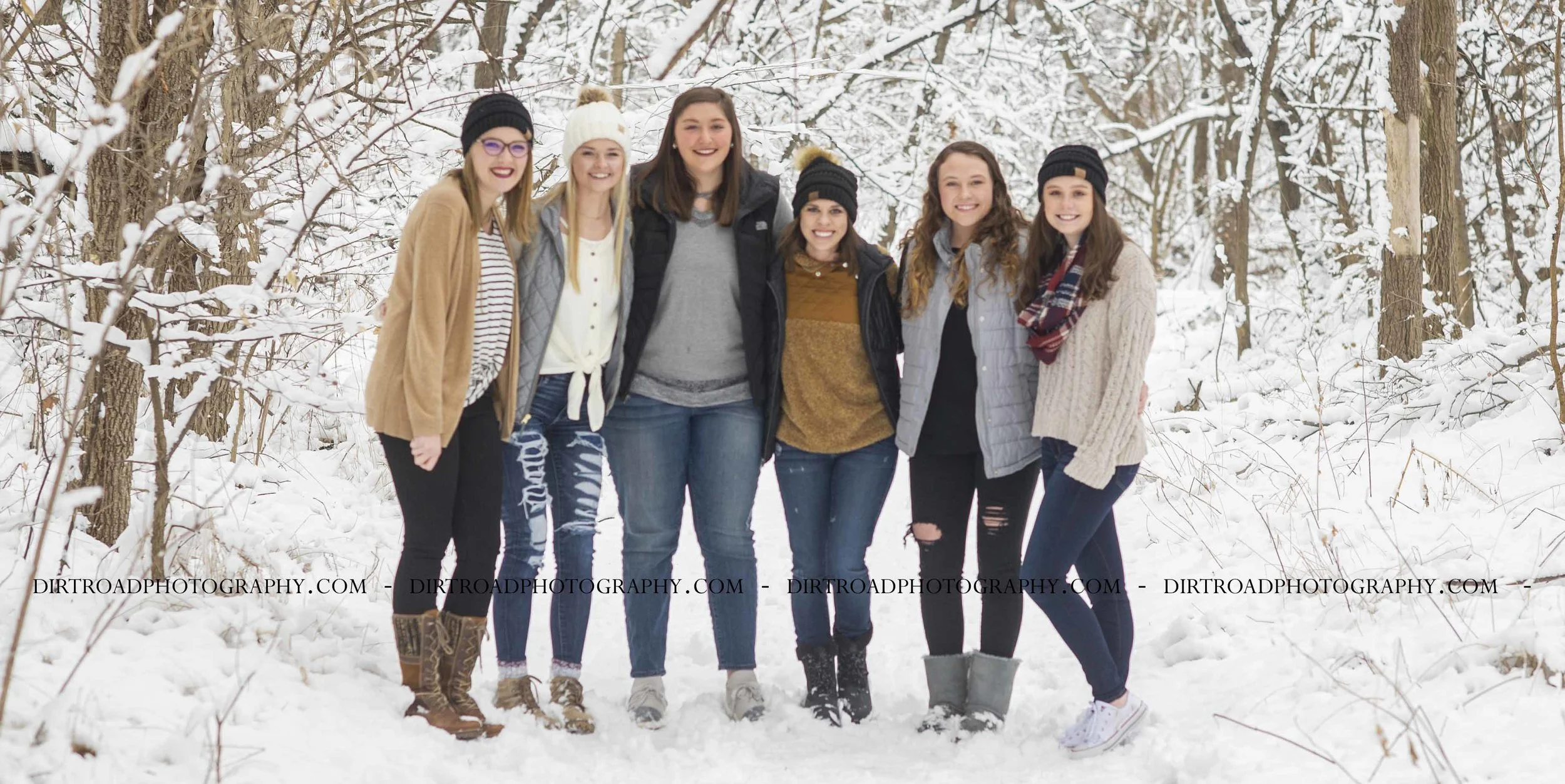 picture of high school senior girls from high schools in nebraska including wilber-clatonia high school, milford high school, friend high school, tri-county high school and norris high school. girls are in blue jeans with cream and white sweaters and winter boots, playing in snow with puffer vests and cc beanie caps. girls laughing and taking pictures in snow throwing it in the air for high school photography dirt road photography by kelsey homolka nerud photographer.
