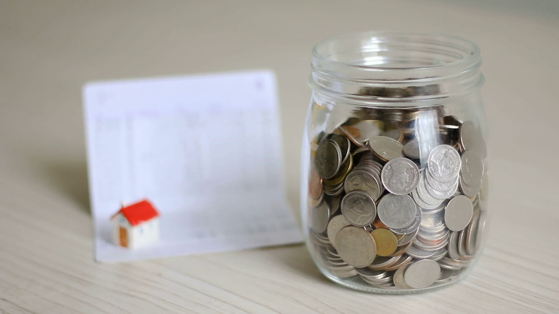 videoblocks-money-coin-falling-into-glass-jar-and-blur-house-and-book-bank-behind-metap_soh-unhcg_thumbnail-full01.png