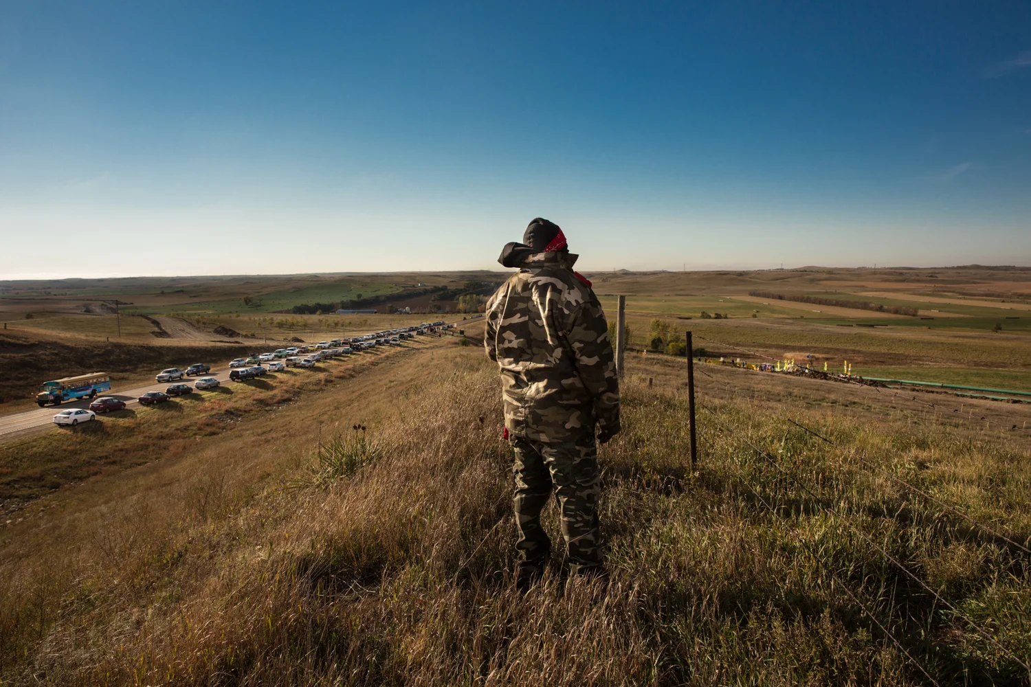 An activist on the lookout on a hill overlooking Job Site 118 near St. Anthony, North Dakota. To his left are cars belonging to native land and environmental rights activists which are parked on a public road. To the right is DAPL Job Site 118 where an Eagle & Condor Ceremony was taking place. Oct. 10, 2016