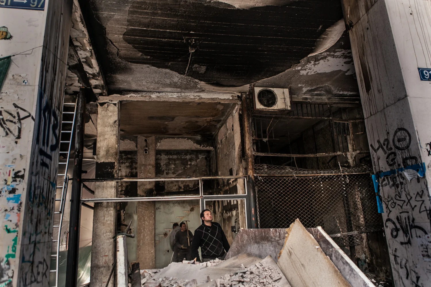 Men inspect damage to a storefront property in downtown Athens after the riot incited by demonstrations against austerity measures proposed by the EU. Athens, Greece. Feb. 17, 2017