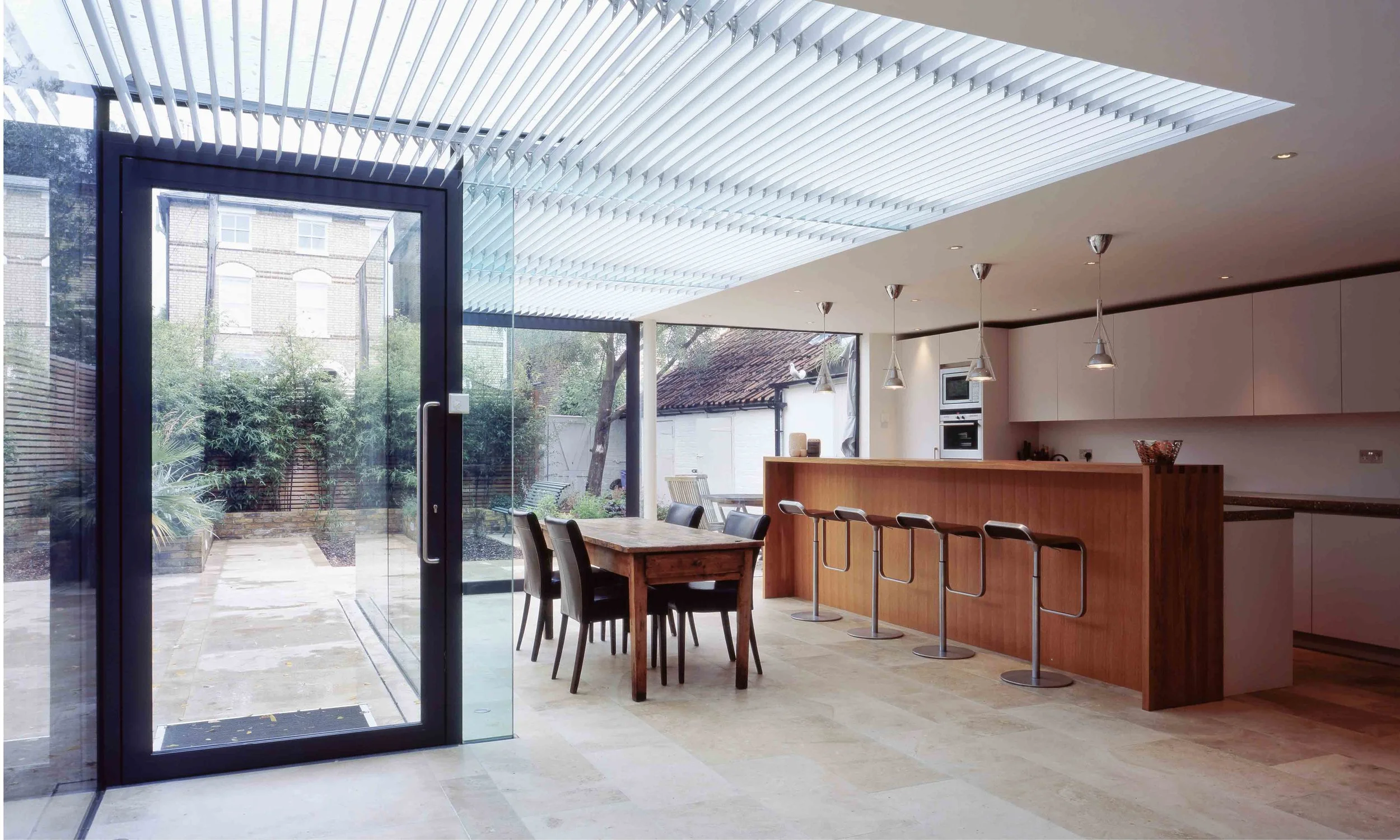 This modern glass extension brings the kitchen and garden together. Mechanical louvres track the sun reduce solar glare. The extension is construction entirely from glass, including the beams and columns.