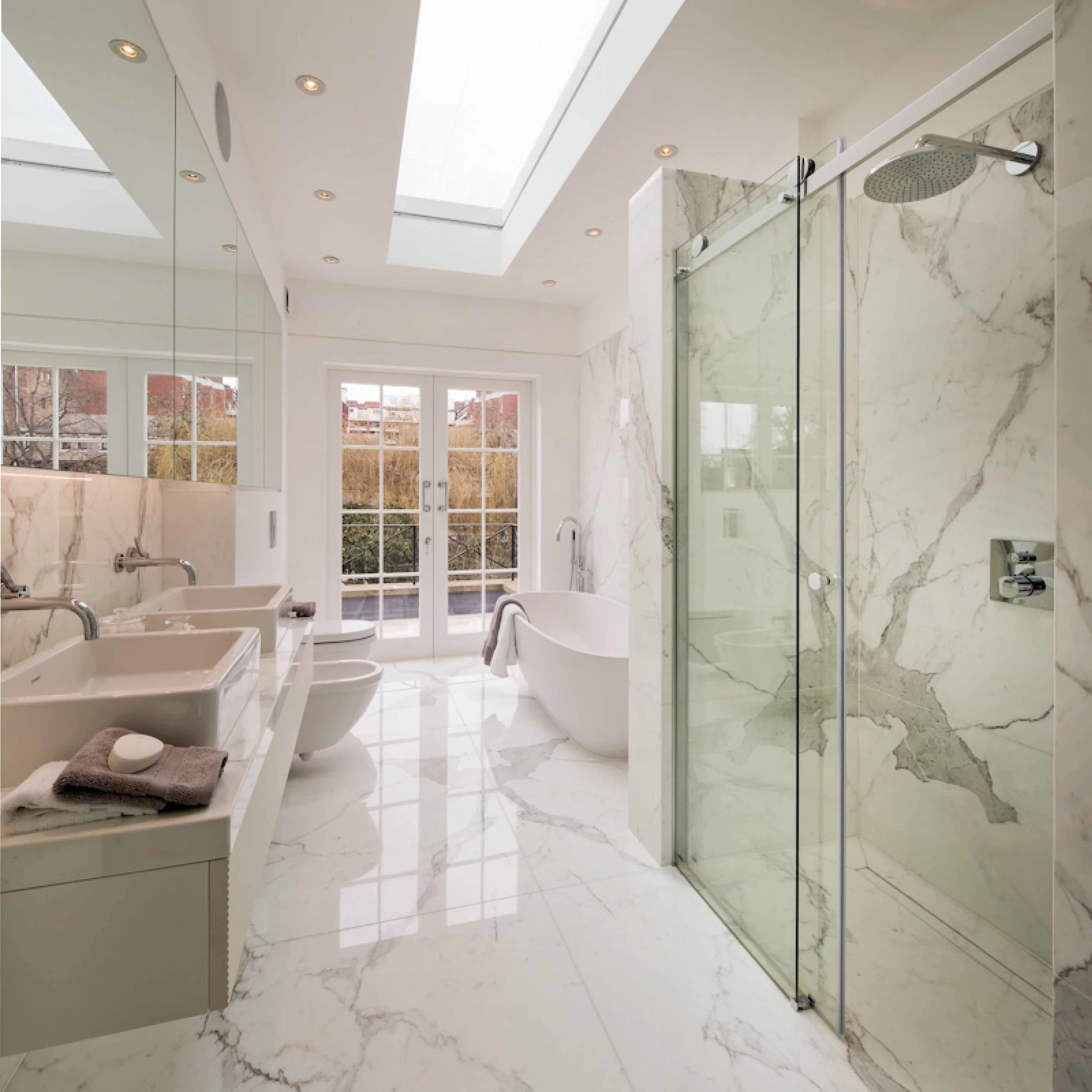 The modern and spacious bathroom. Book matched marble walls and floors are light by a contempoary roof light creating a luxurious space, 