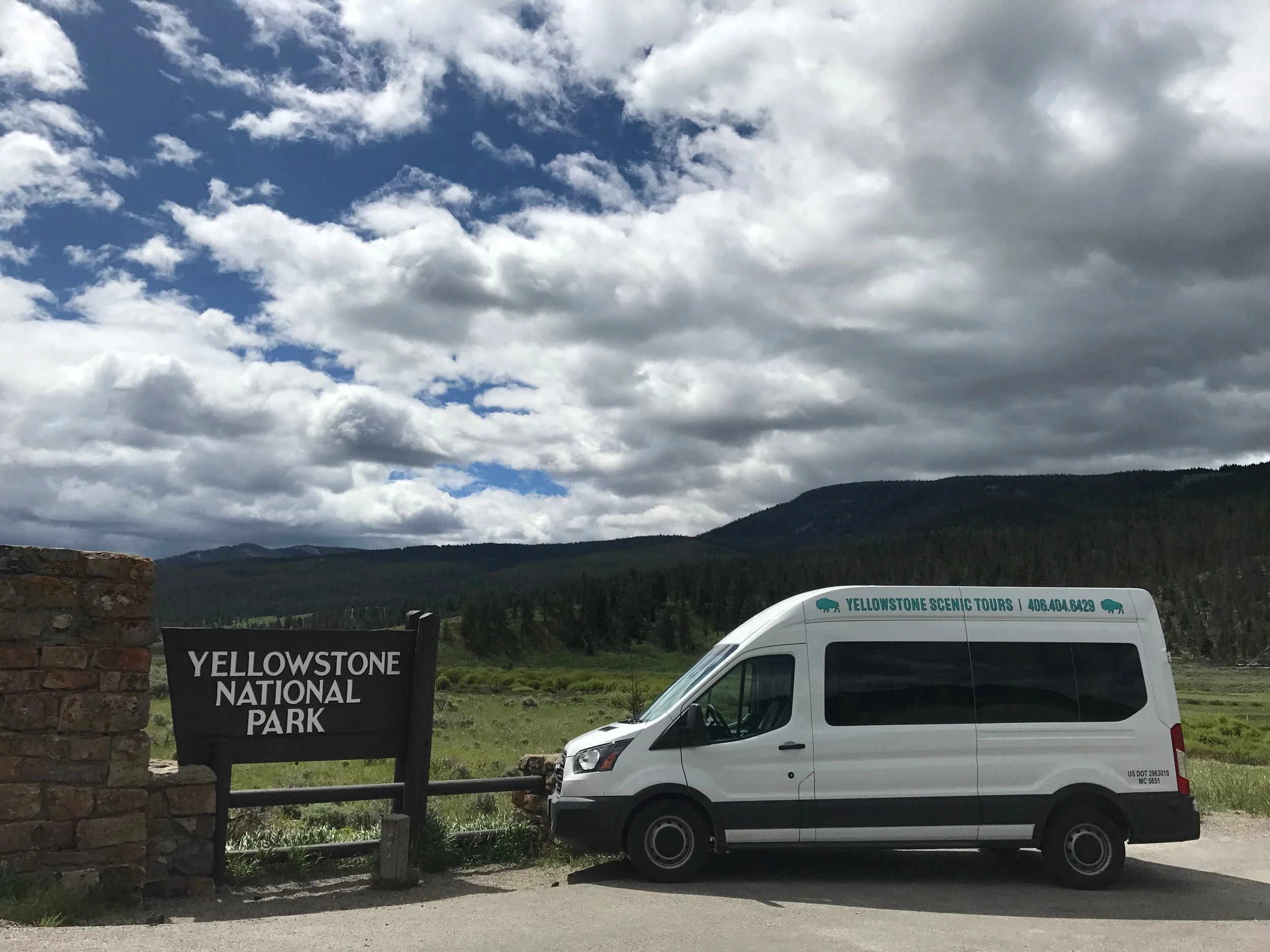 Photo of the Yellowstone Scenic Tours vans parked at the Yellowstone National Park sign.