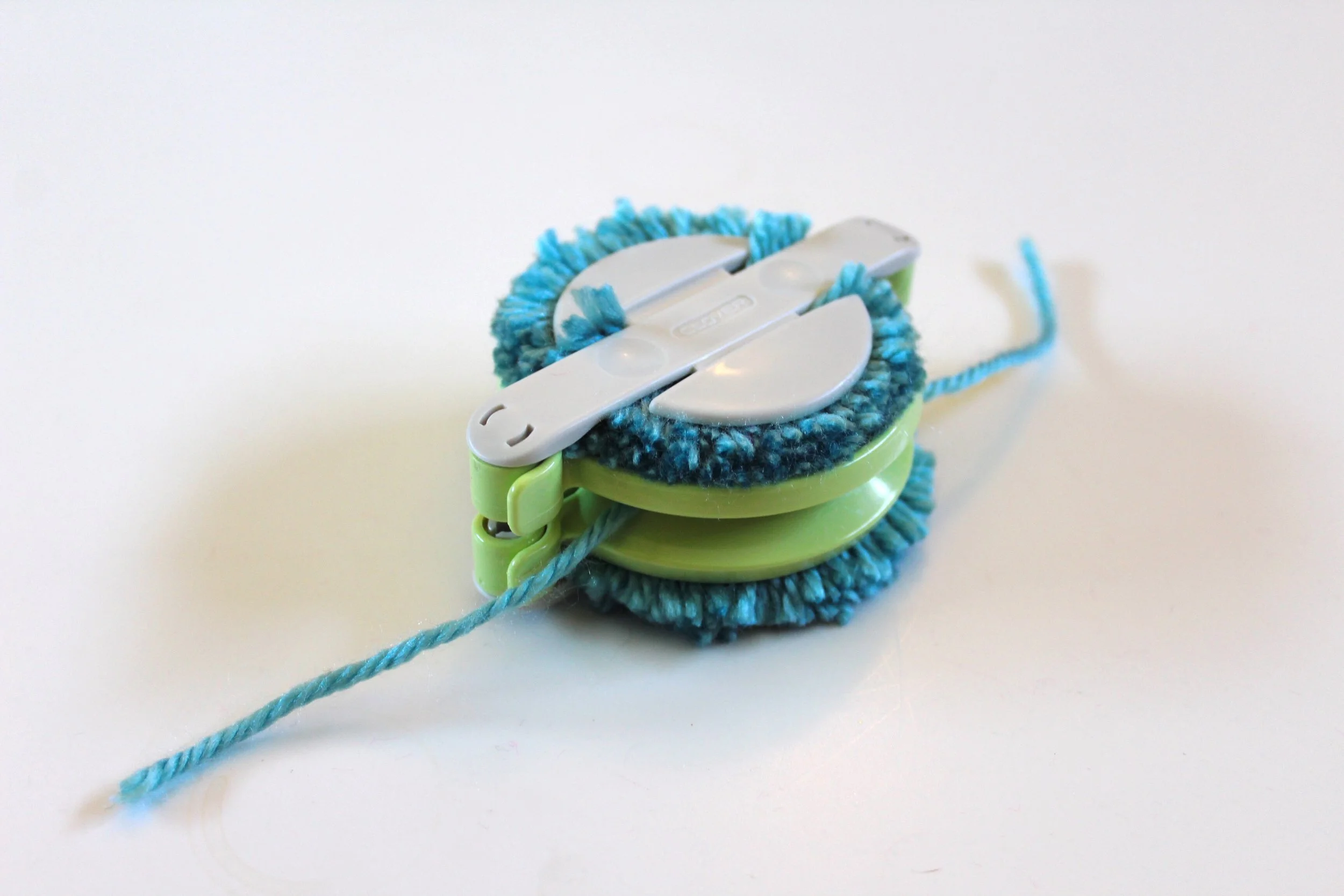 Clover Pom Pom Maker. Yarn has been cut and yarn tied to keep the pom pom together. 