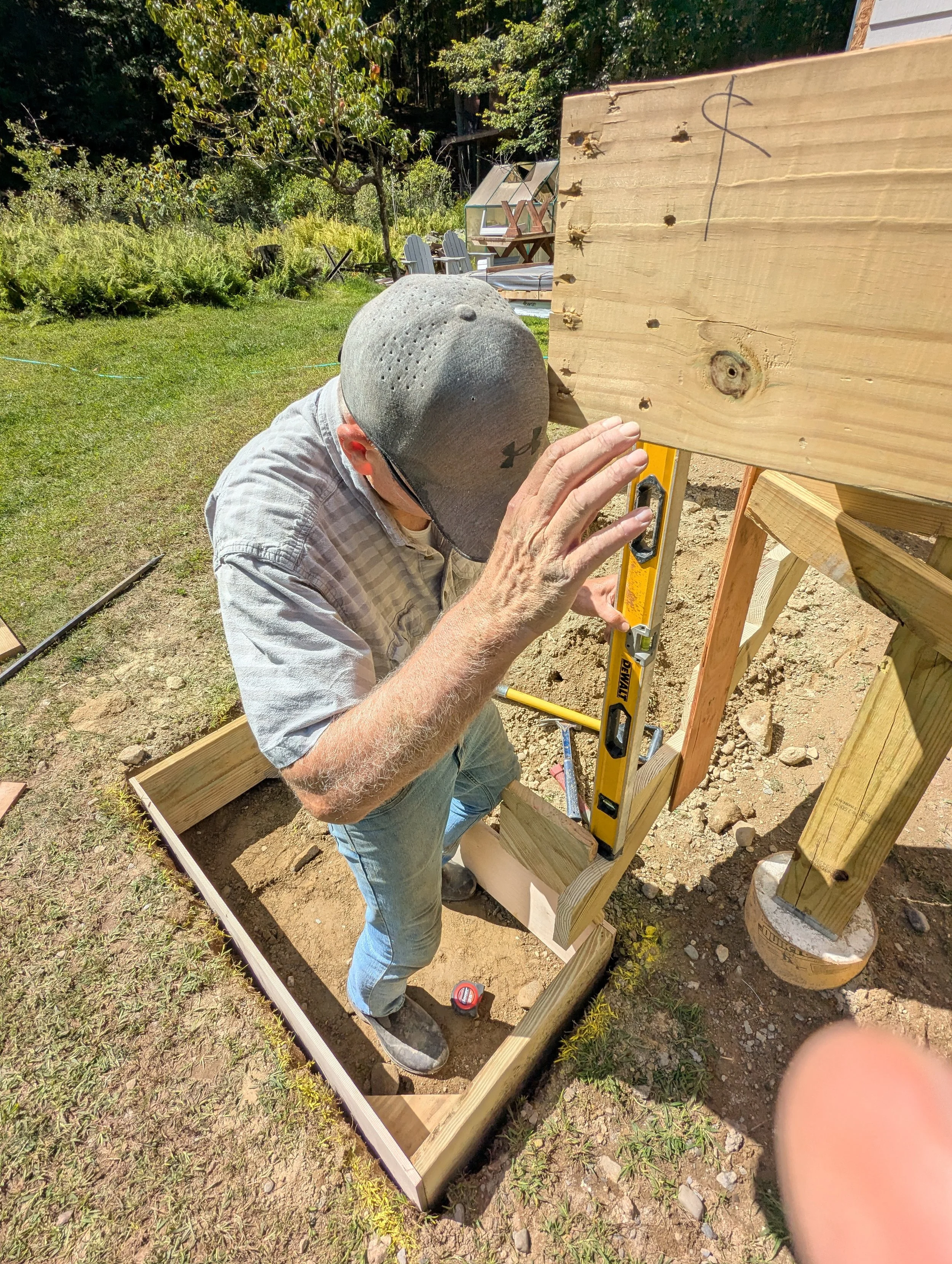 Man wearing a cap uses a level to align a wooden structure during backyard construction.