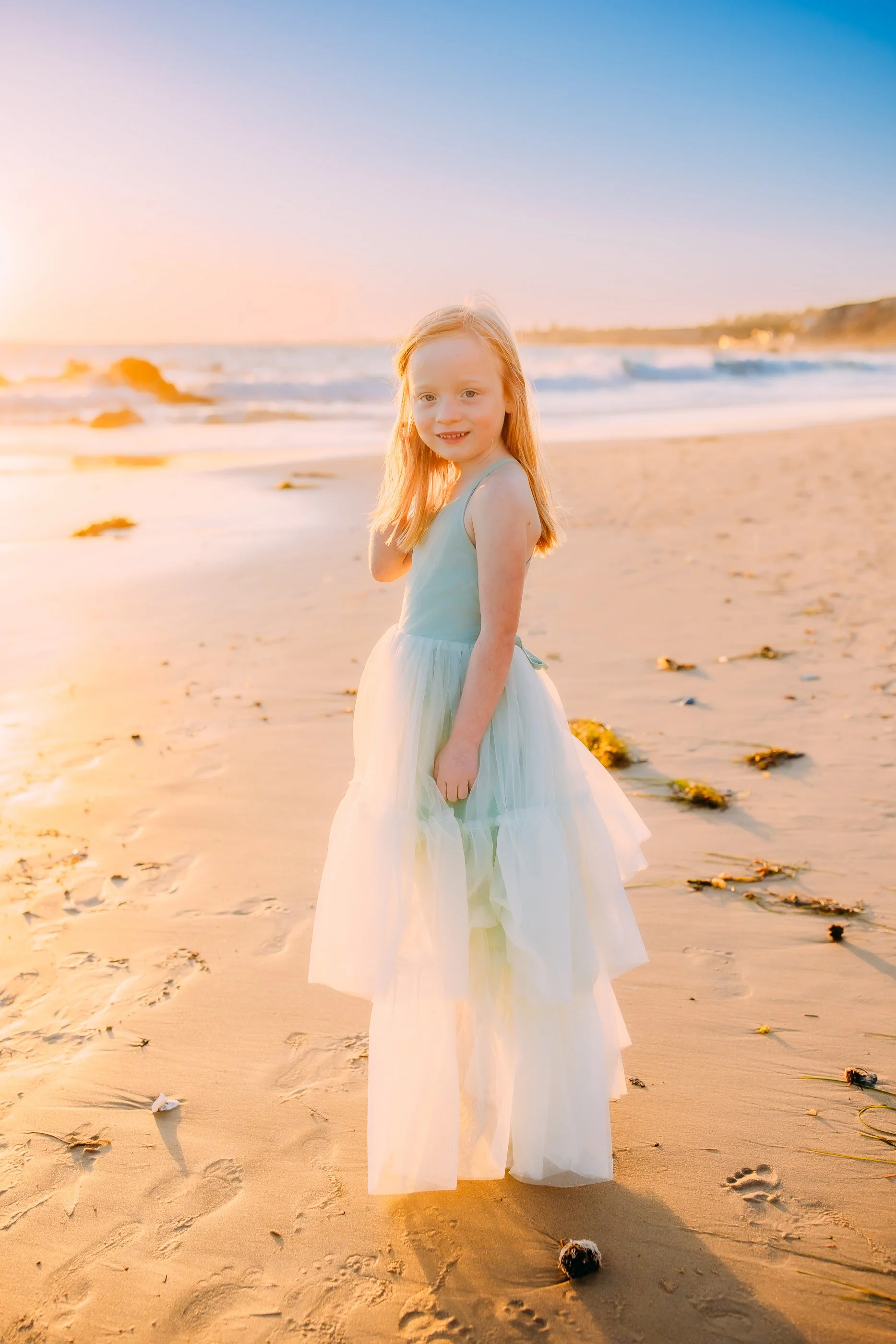 girl smiling at the camera with the ocean behind her during her family photoshoot in Newport Beach, California