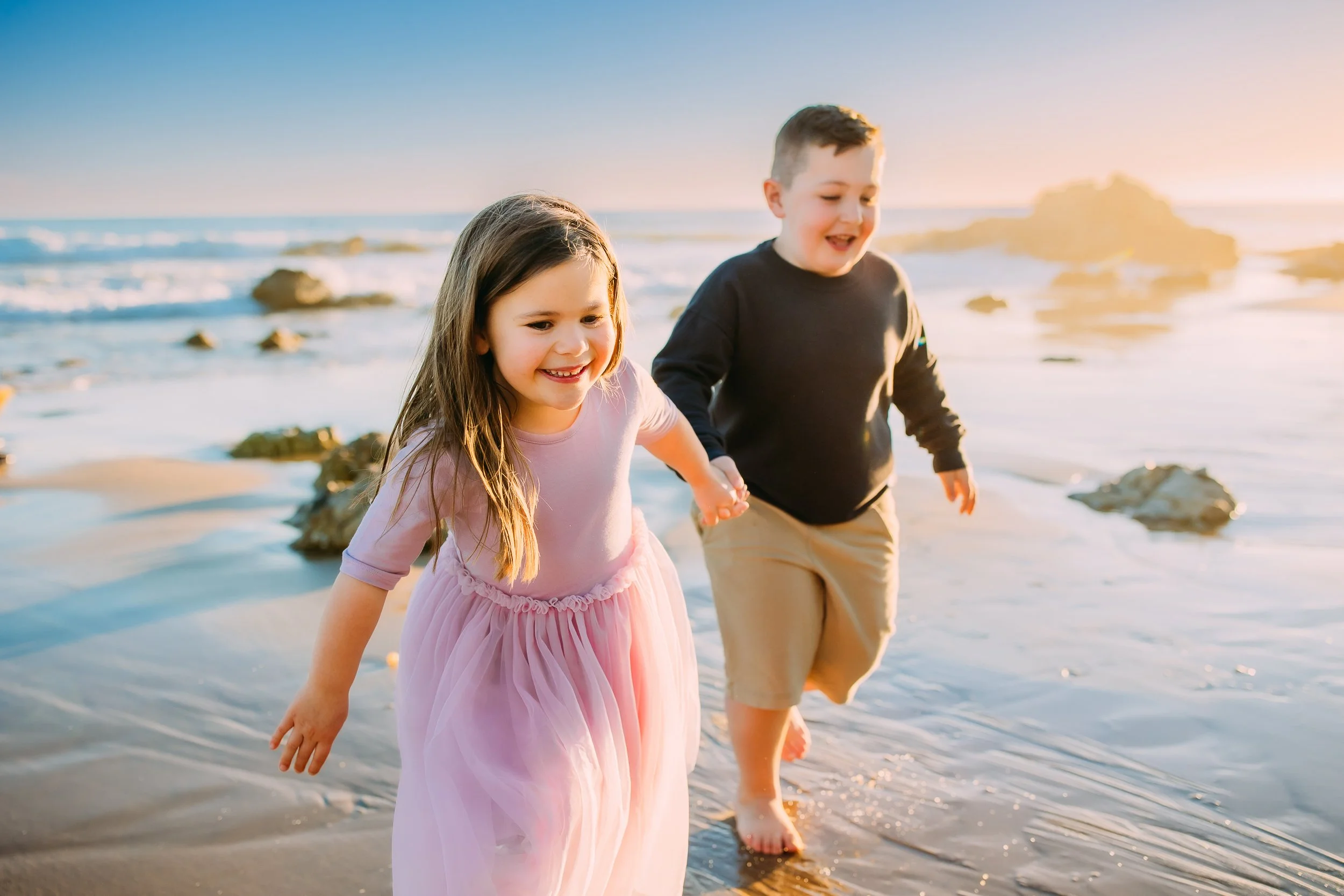 brother and sister happily running along the shoreline in Newport Beach
