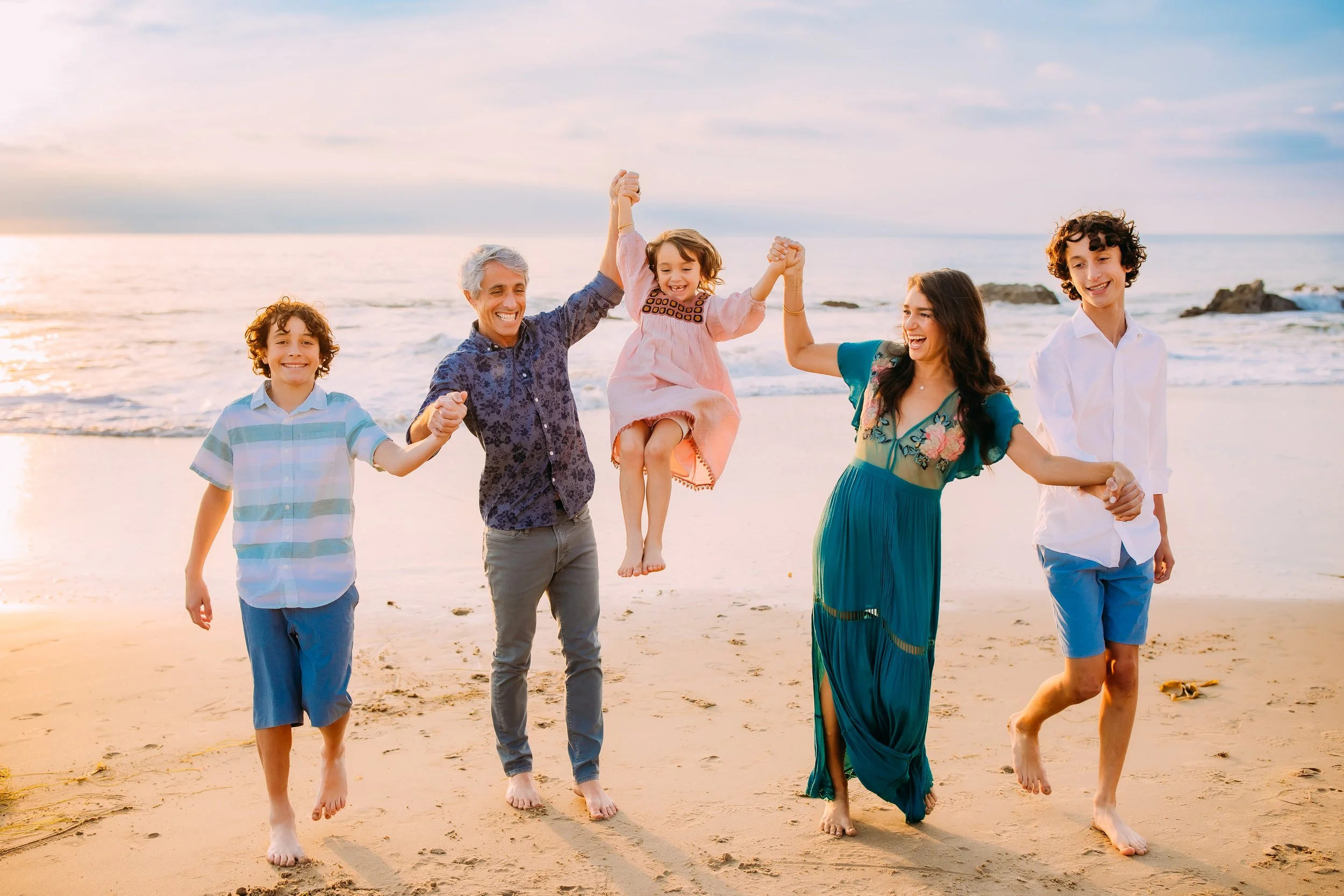 parents swinging their daughter through the air at a beach photo session in Newport Beach, California