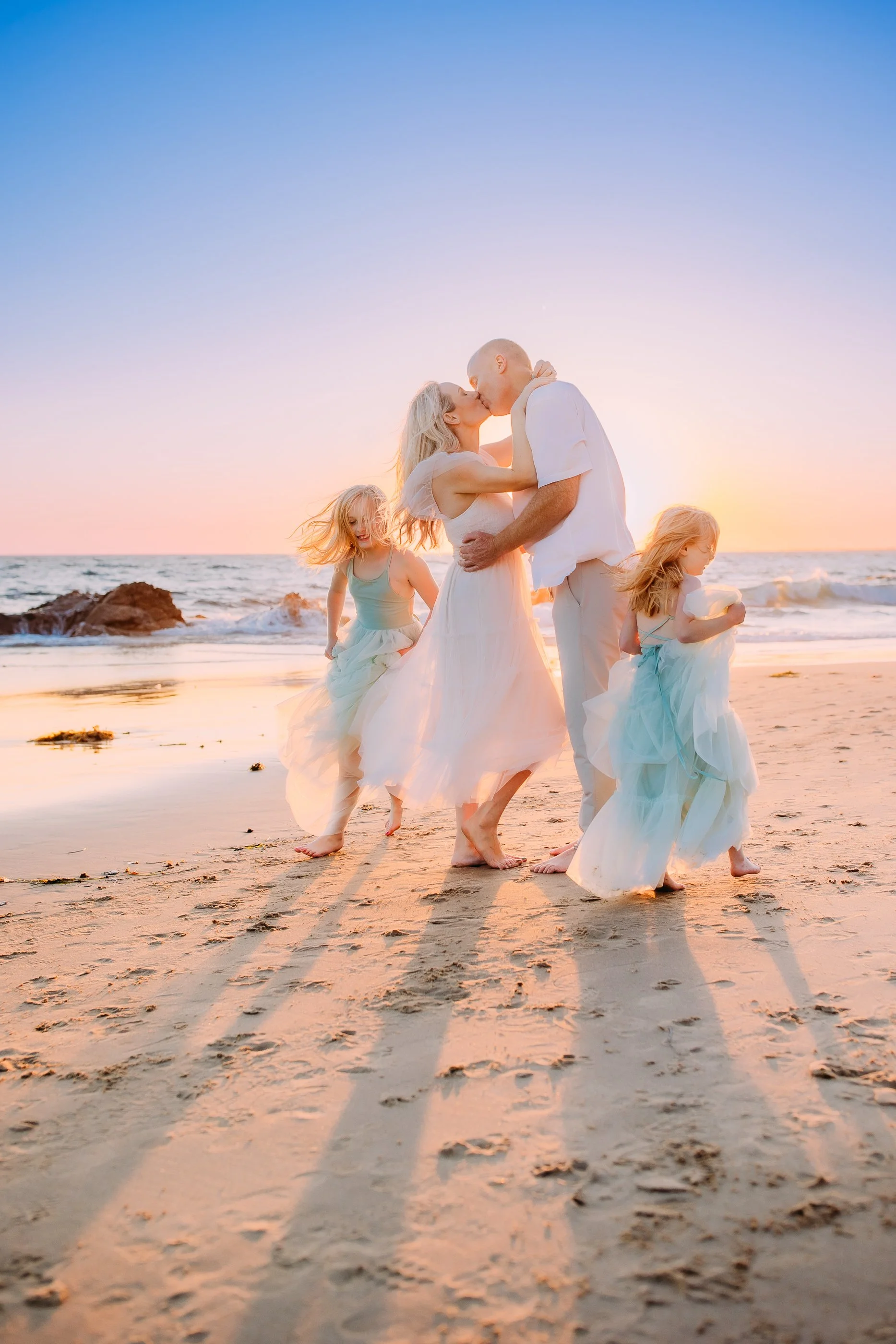 two sisters happily running around their parents during a more candid moment of their photoshoot at Newport Beach, California