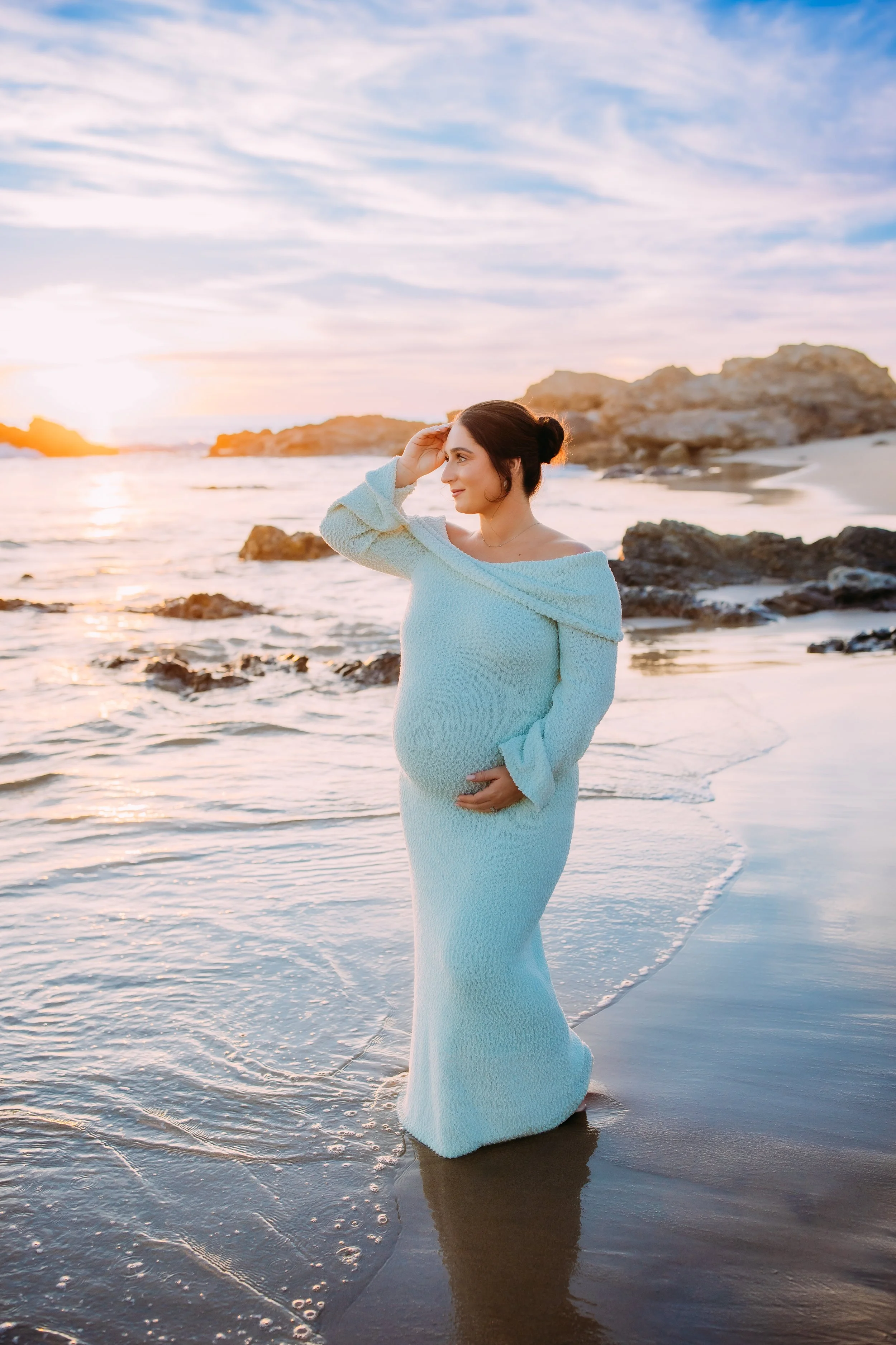 mom to be gazing out at the sunset along the ocean's edge at her maternity photo session in Newport Beach, California