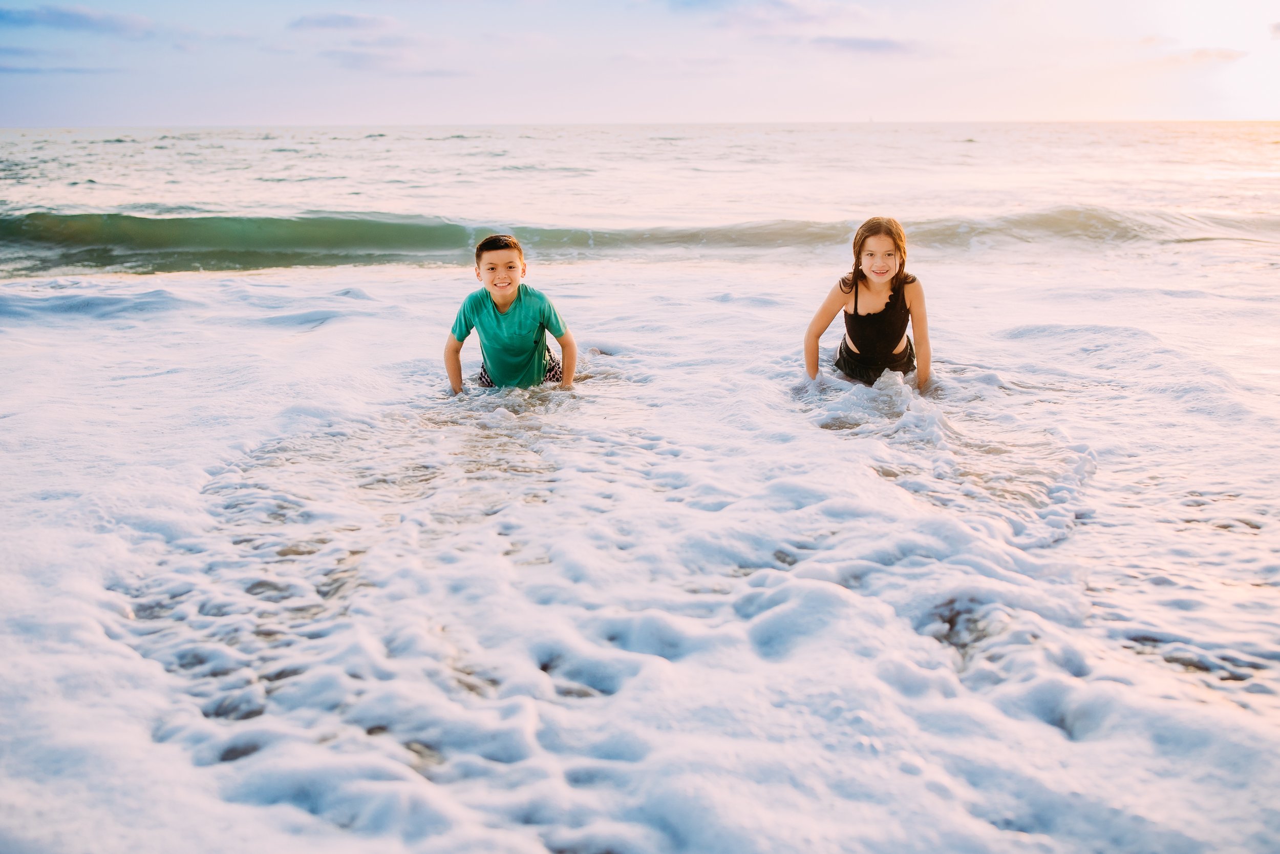 siblings riding their boards in the Ocean during their photoshoot in Newport Beach, California