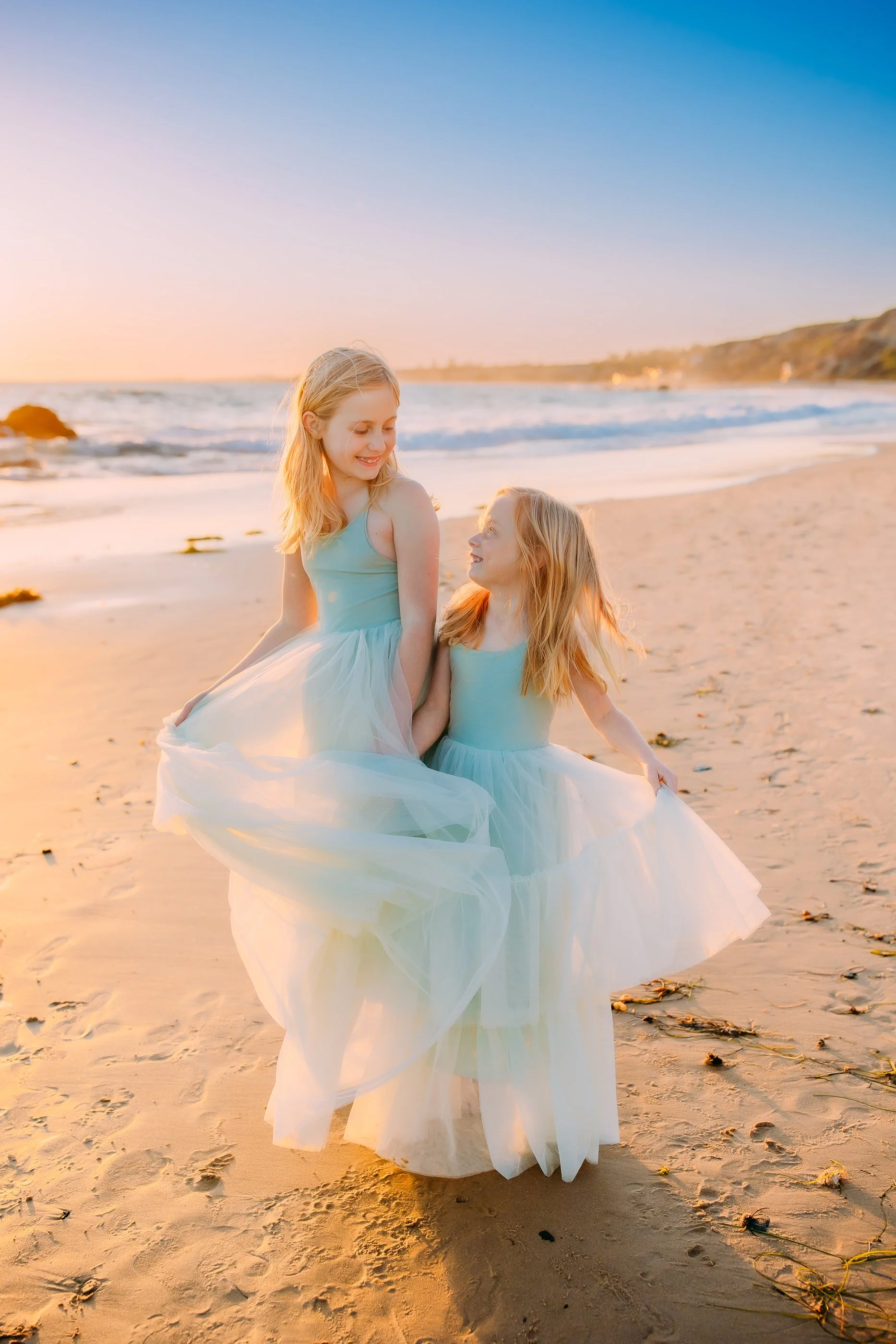Sisters smiling with each other as they twirl their dresses during their family photo session in Newport Beach, California