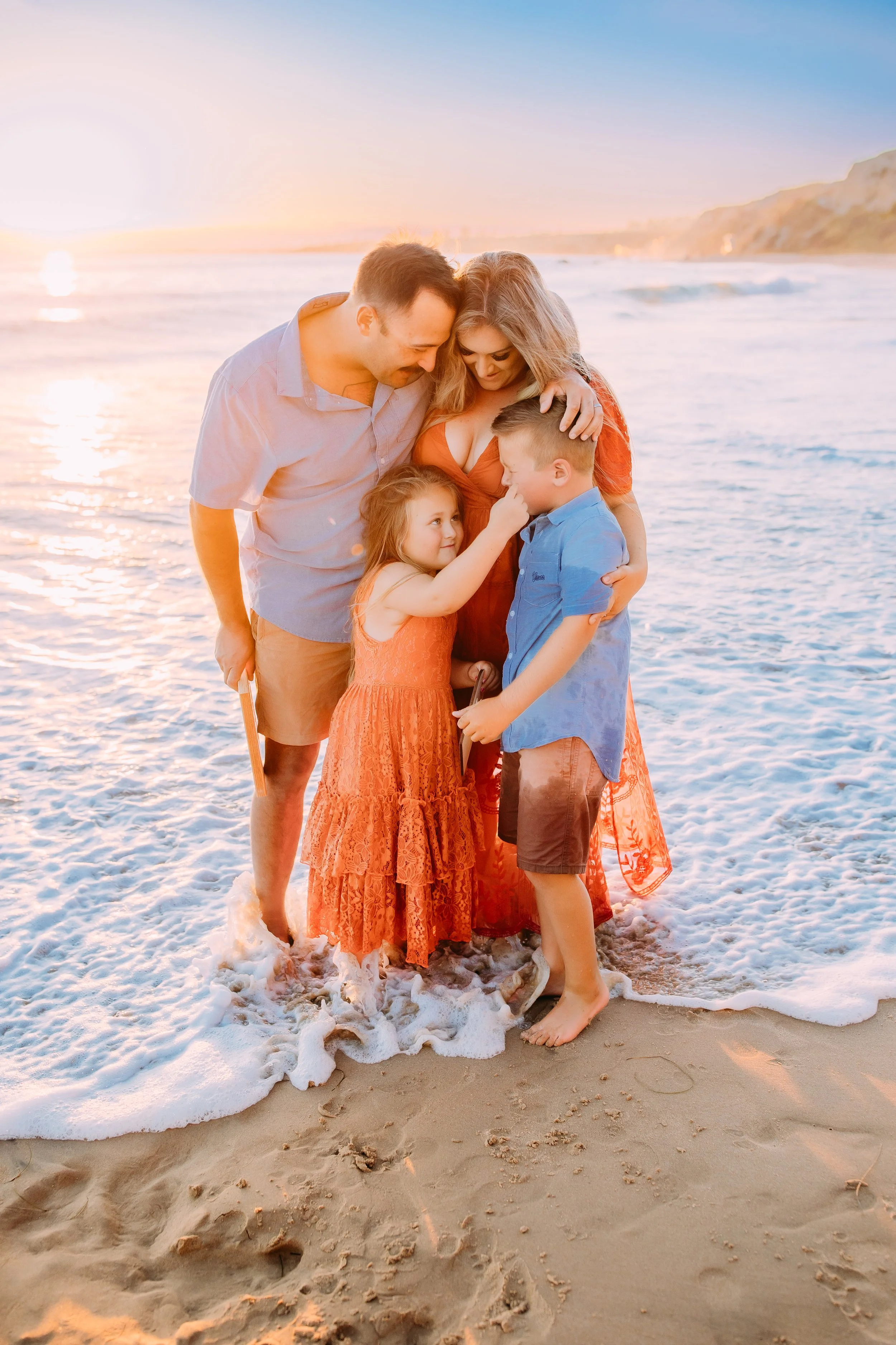 sister wiping her brother's tears after his overwhelming excitement about the new baby announcement during their family photoshoot in Newport Beach, California