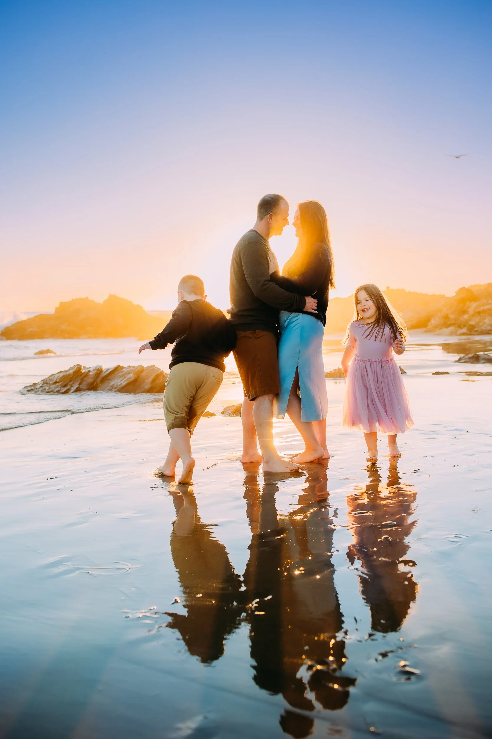 kids joyfully running around their laughing parents during their glowing sunset photoshoot in Newport Beach.