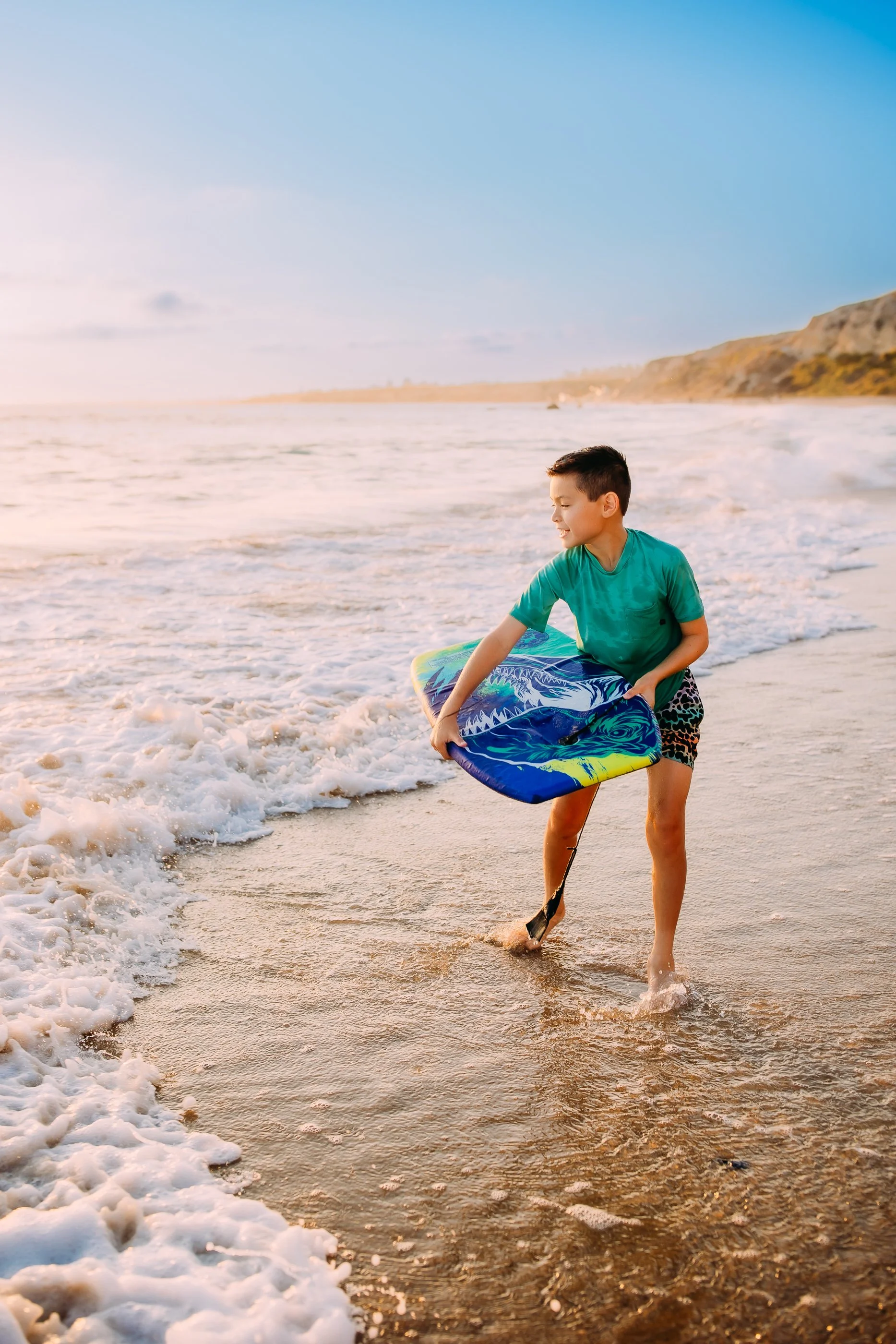 boy about to run into the surf with his board during his family photo session at sunset in Orange County, California