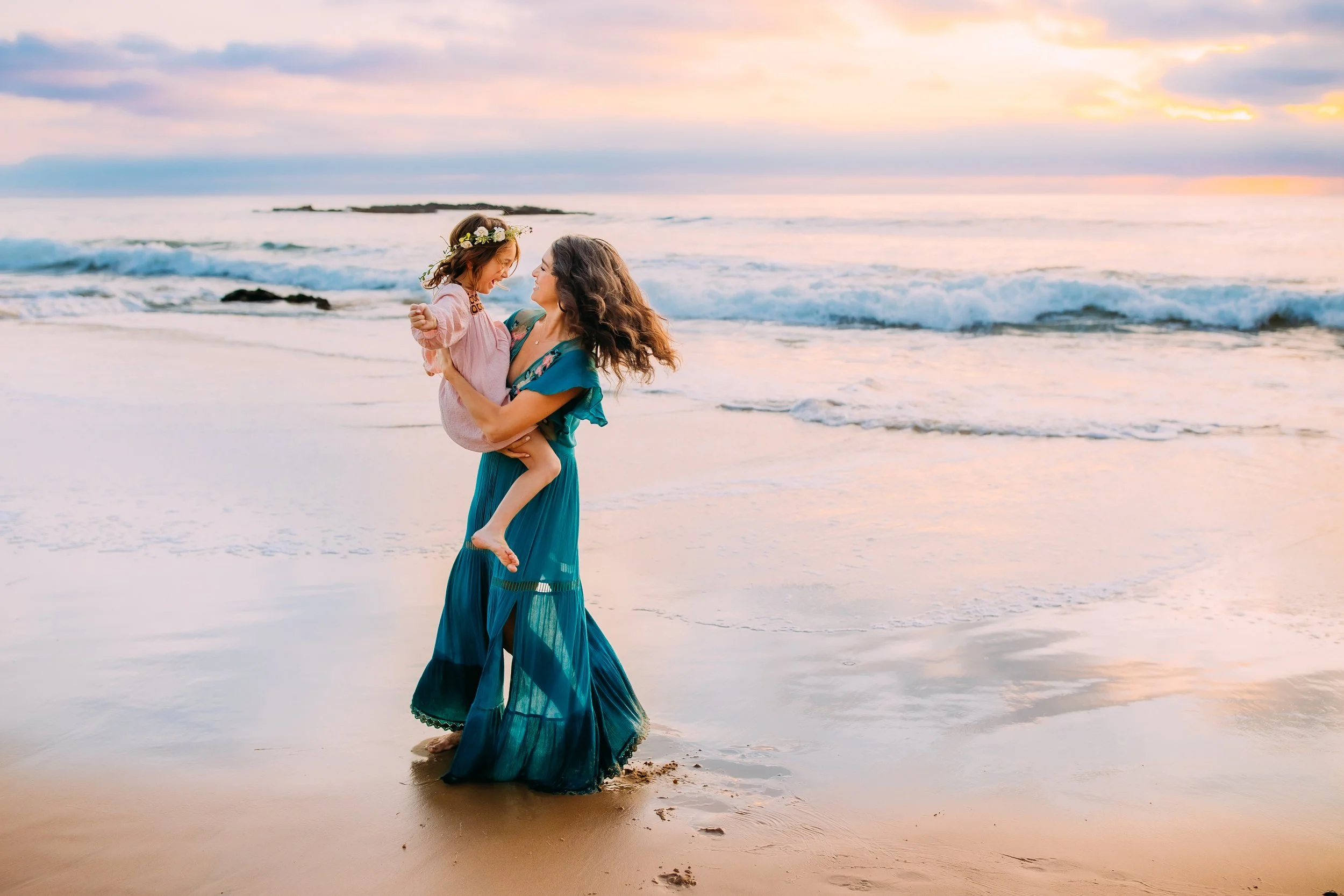 mom playfully spinning and dancing with her daughter in the ocean tide in Newport Beach, Califnornia